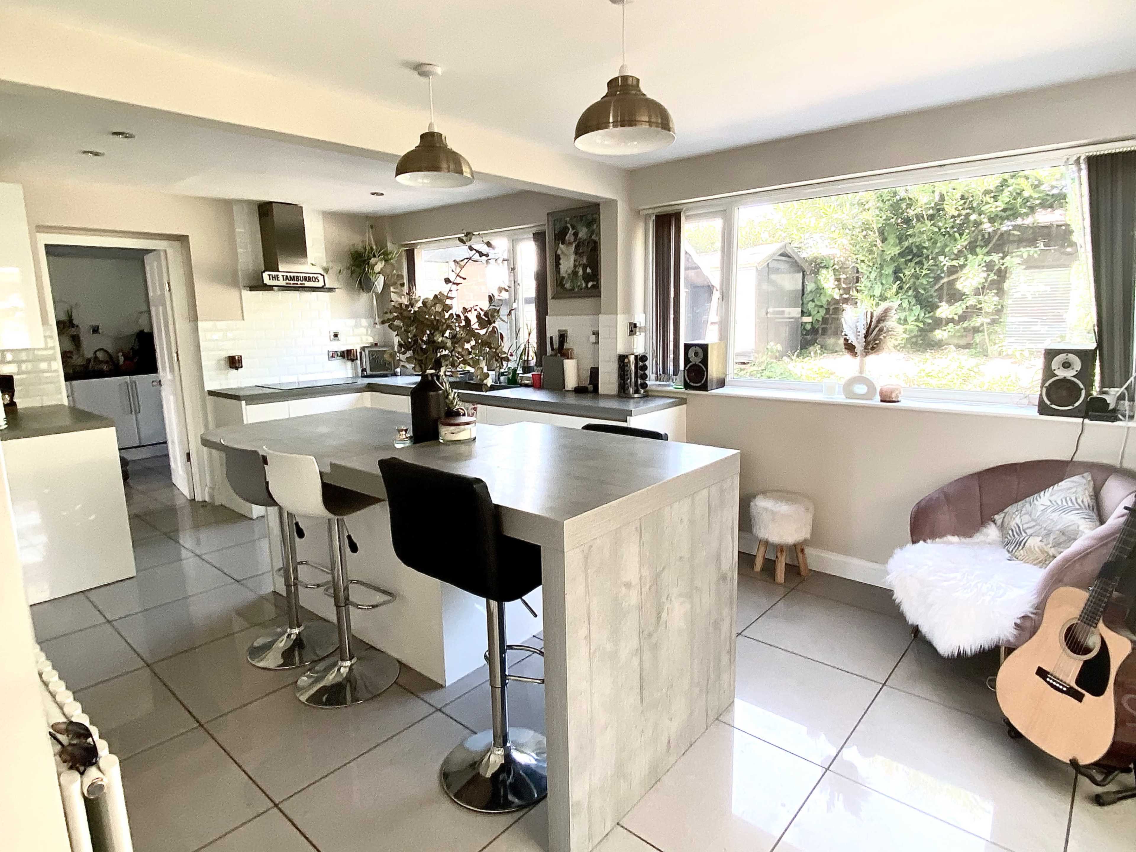 A modern kitchen with a large island, bar stools, and a cozy seating area with a guitar.
