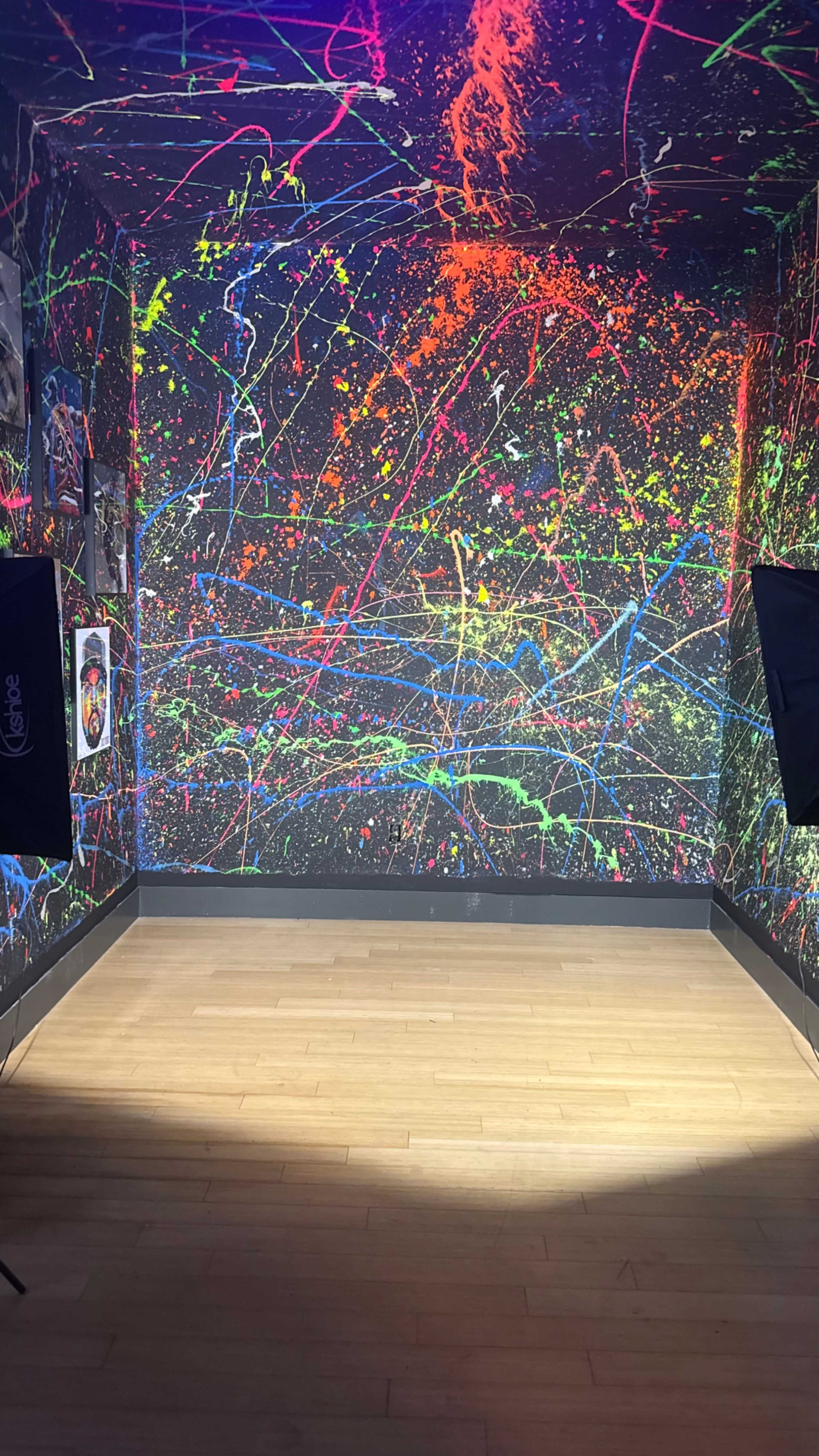 The image shows a room with a brightly painted wall featuring colorful splashes and streaks of paint, illuminated by soft lighting.