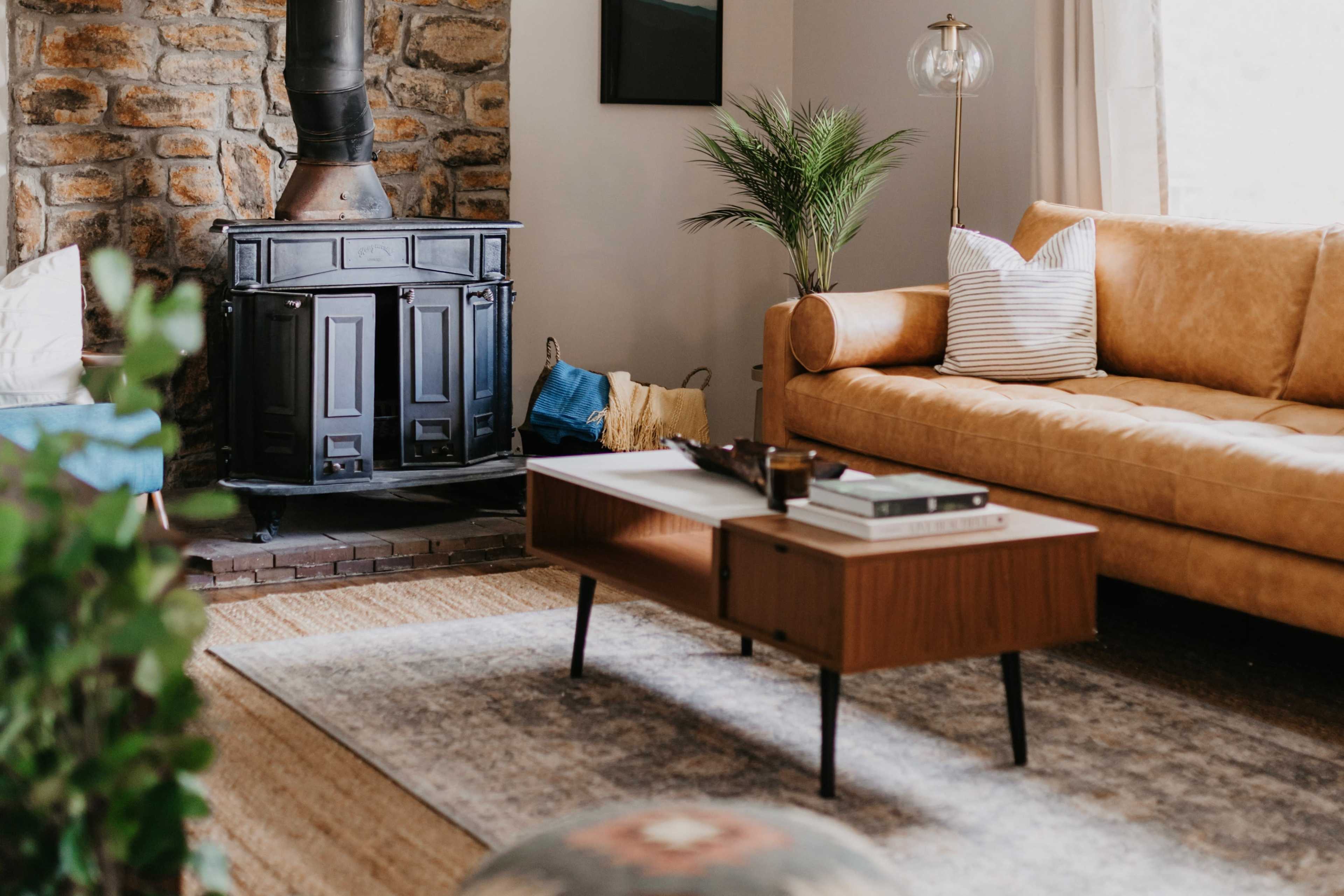 A cozy living room features a leather sofa, a wooden coffee table, and a stone fireplace with a metal stove.