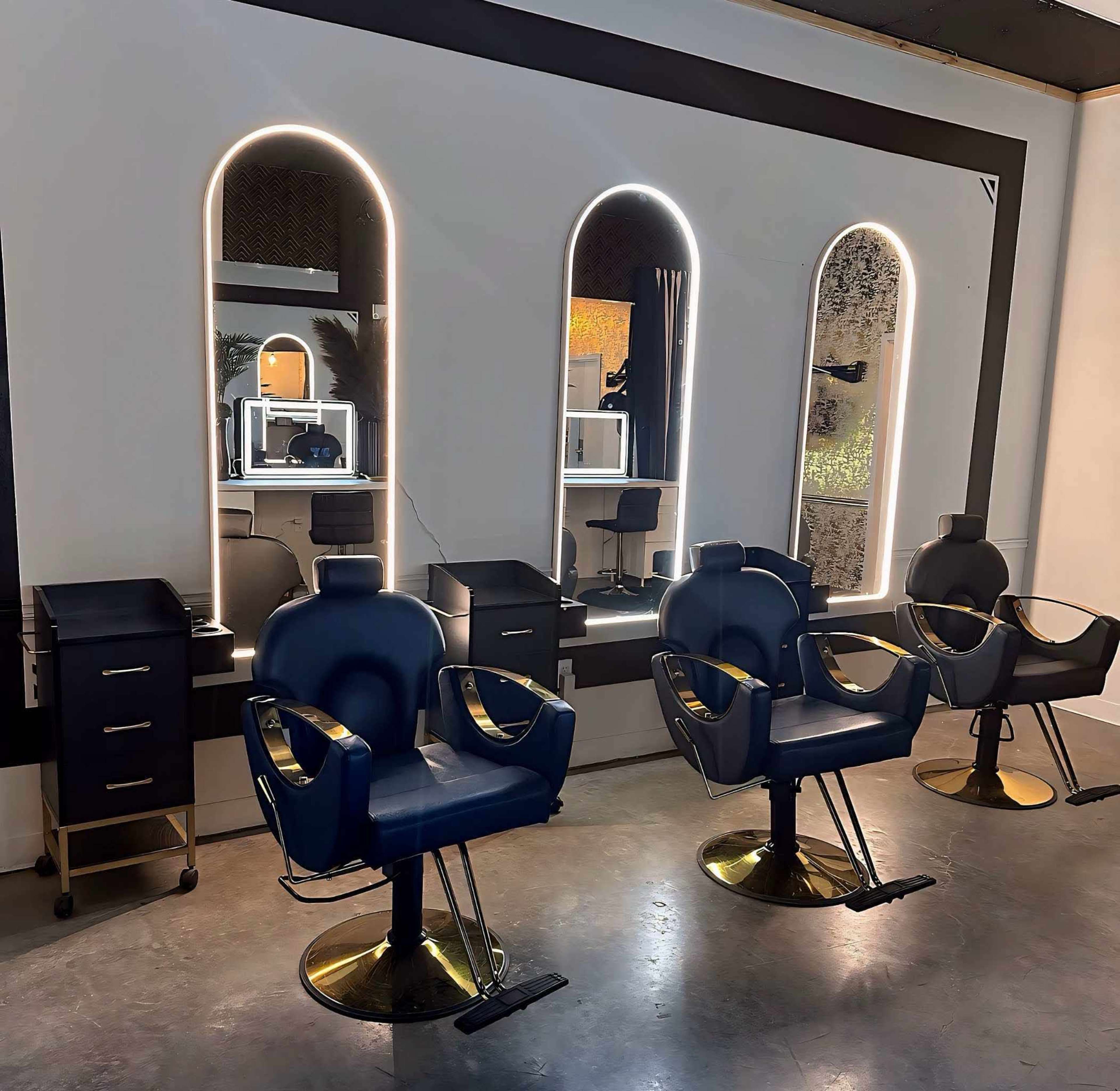 The image shows a hair salon with three stylish barber chairs positioned in front of a large mirror, accented by three arch-shaped frames with illuminated edges.
