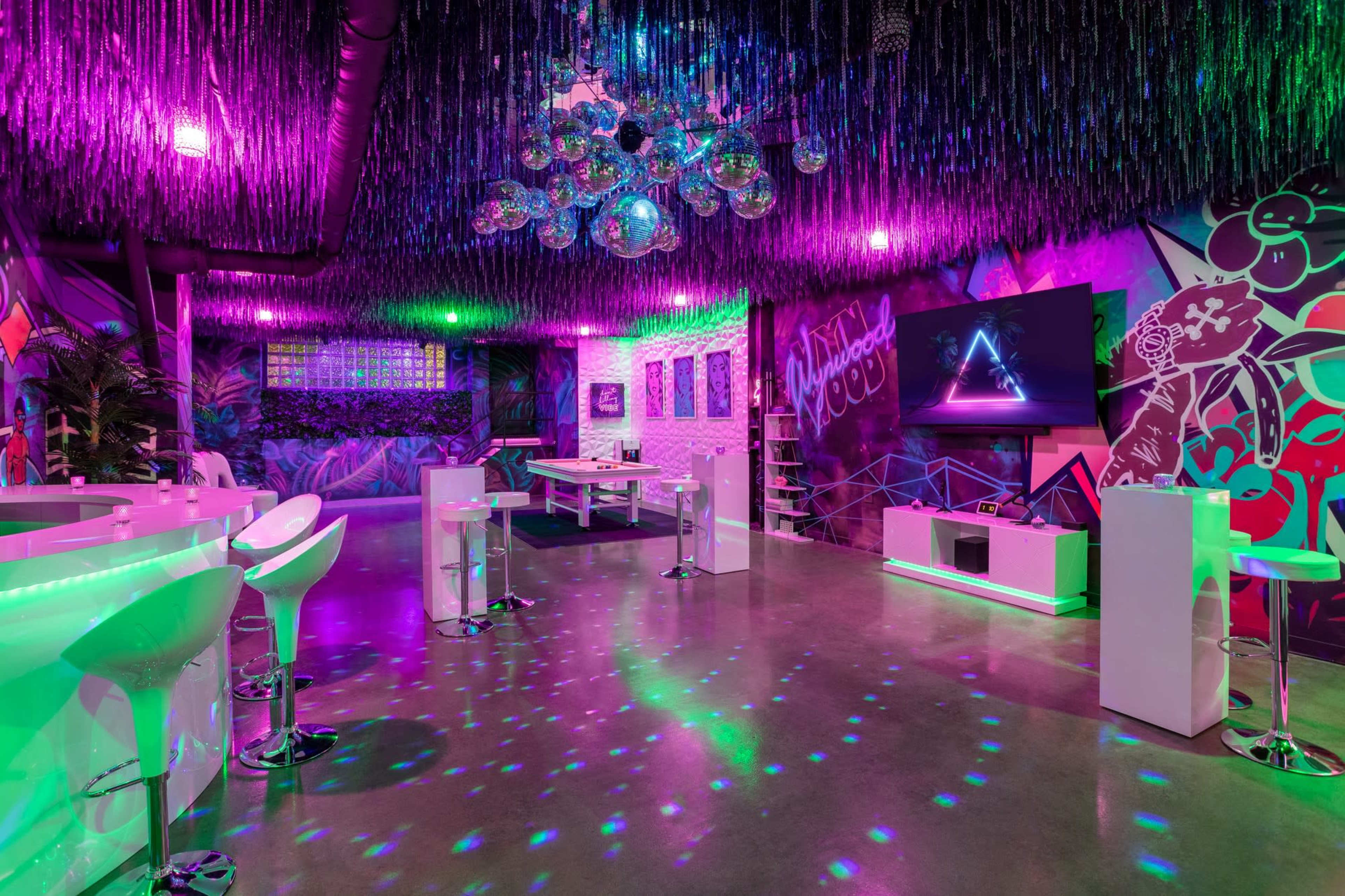 A vibrant lounge space with colorful lighting, a disco ball, and modern furniture against a decorated wall.