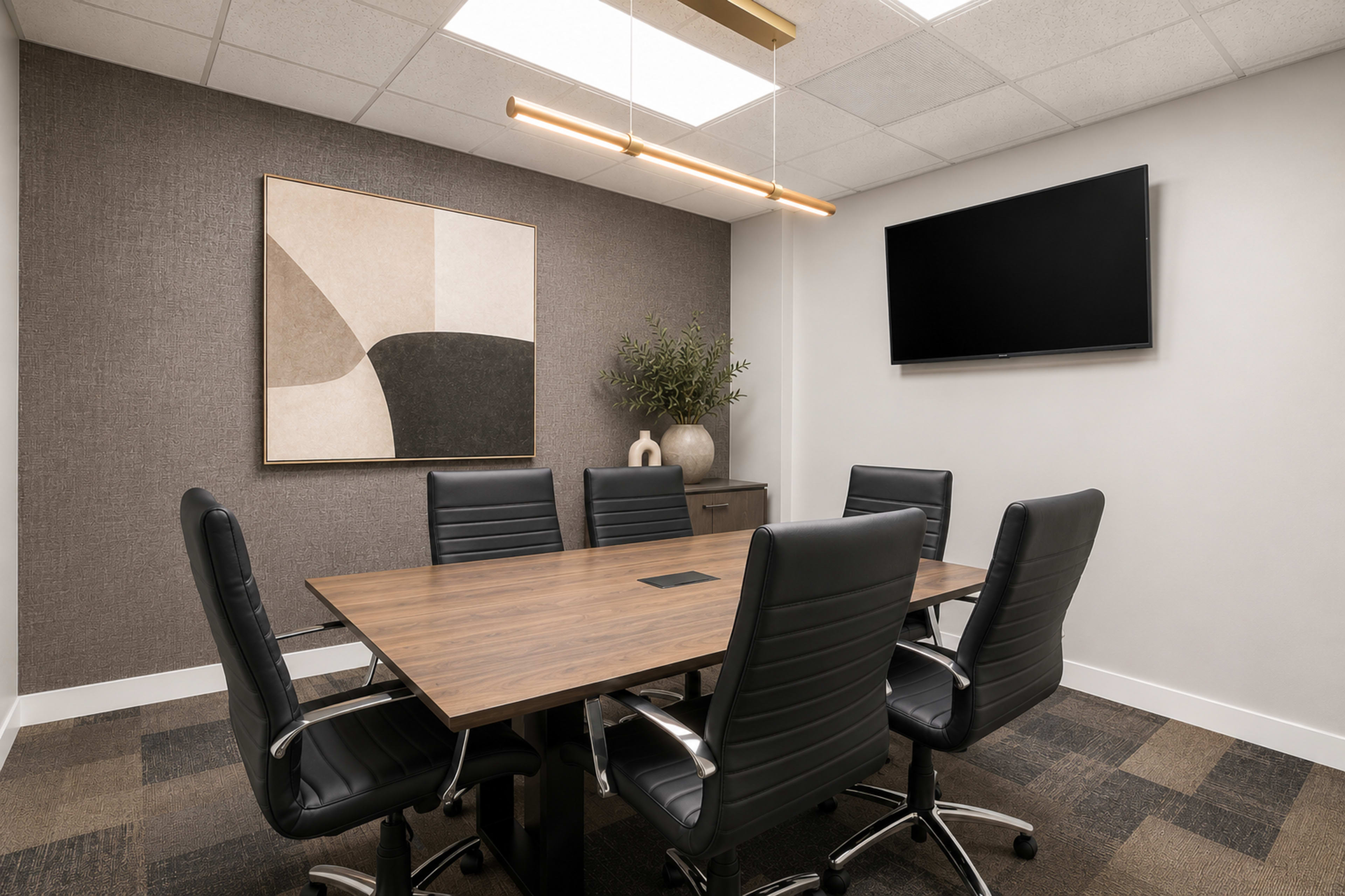 A modern conference room features a rectangular wooden table surrounded by black leather chairs, a wall-mounted television, and an abstract art piece.
