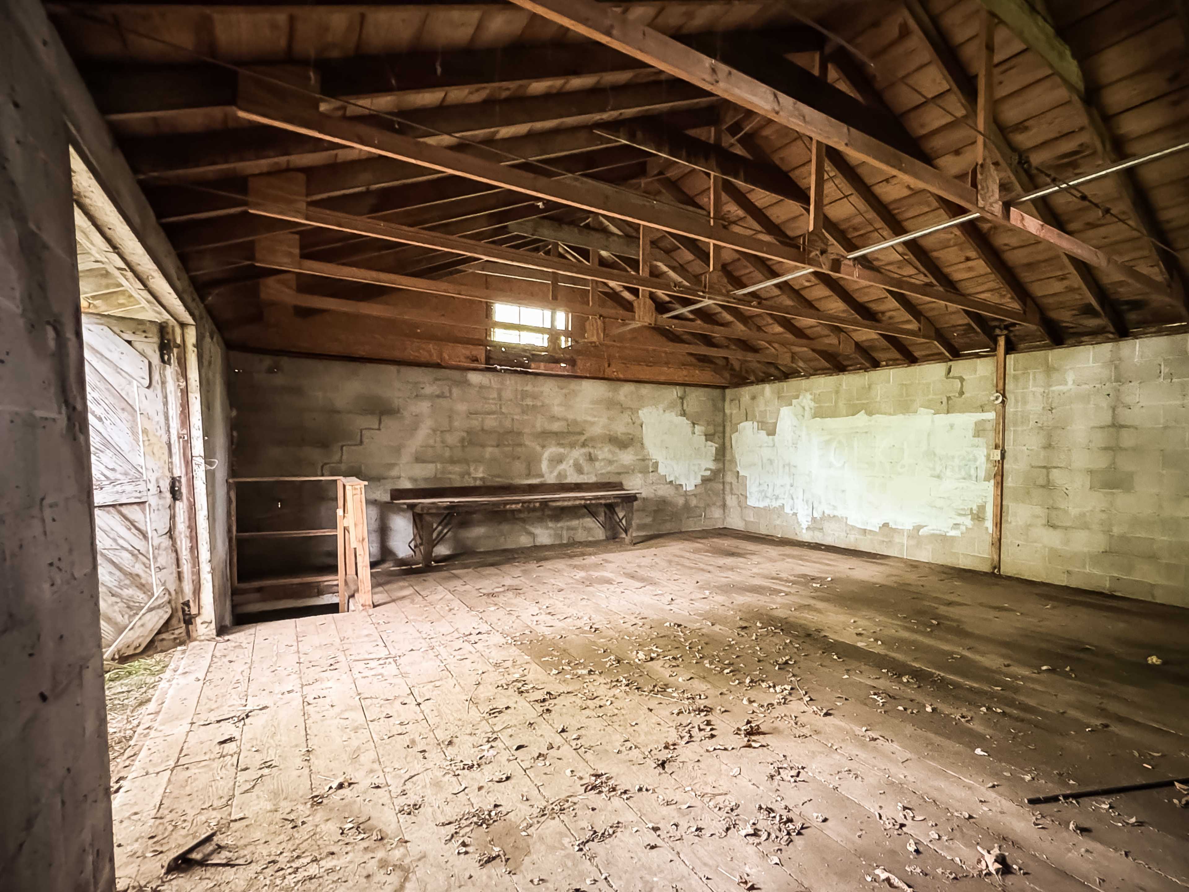 The interior of a rustic, empty barn with wooden beams and a concrete block wall.