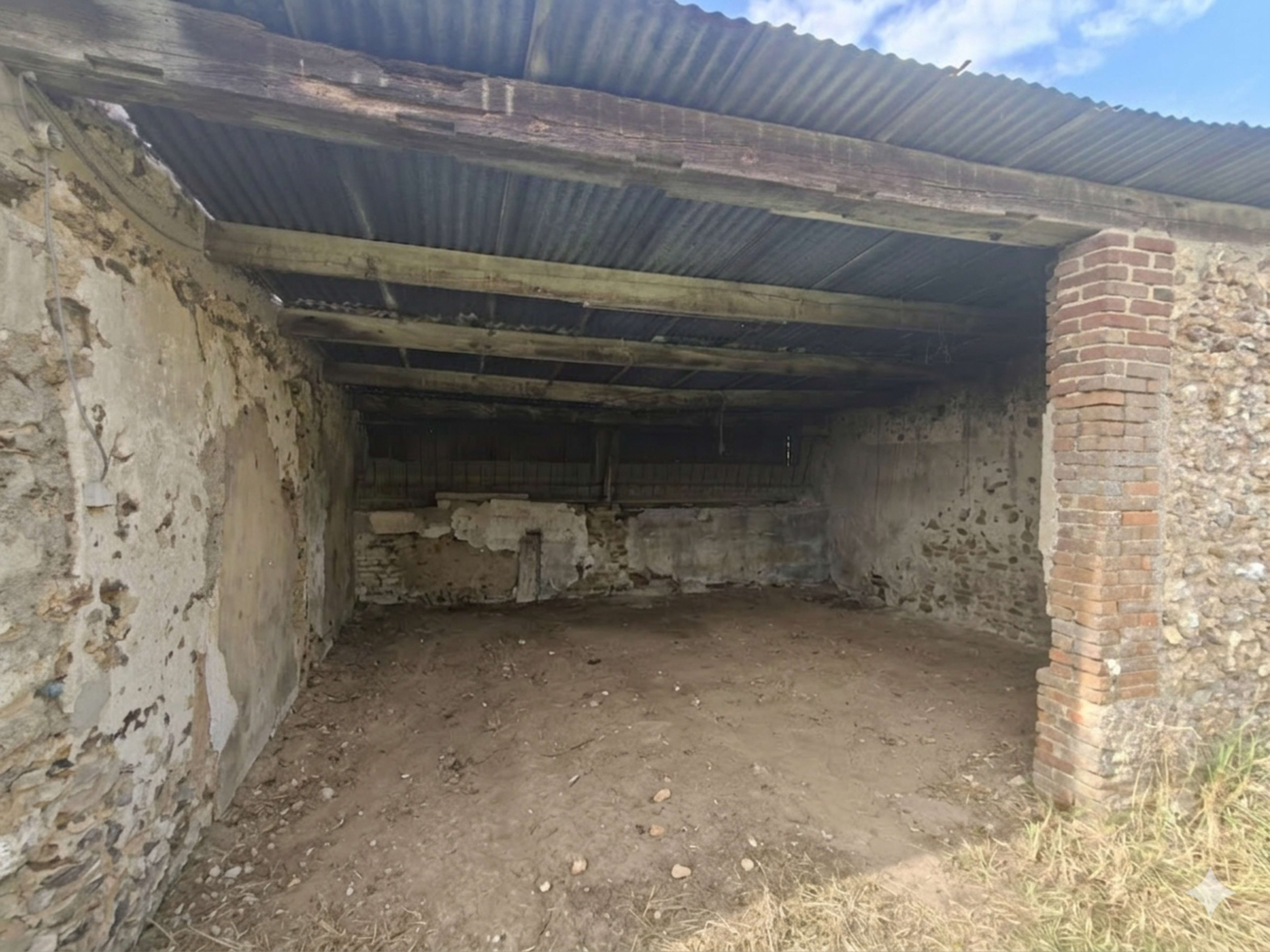 The image shows an empty, weathered storage shed with exposed brick and stone walls, covered by a corrugated metal roof.