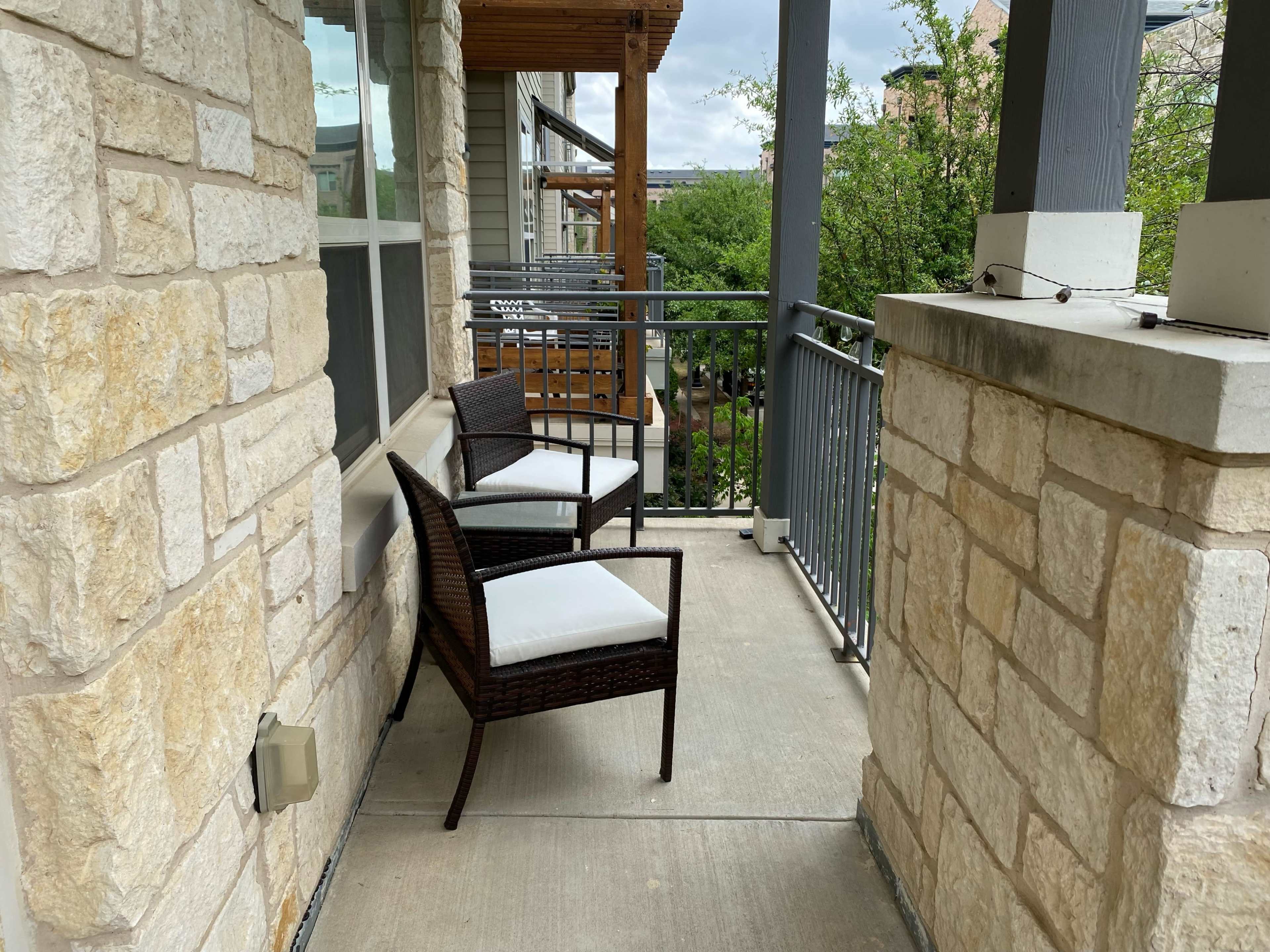The image shows a small balcony with two chairs positioned against a stone wall, overlooking a green area.