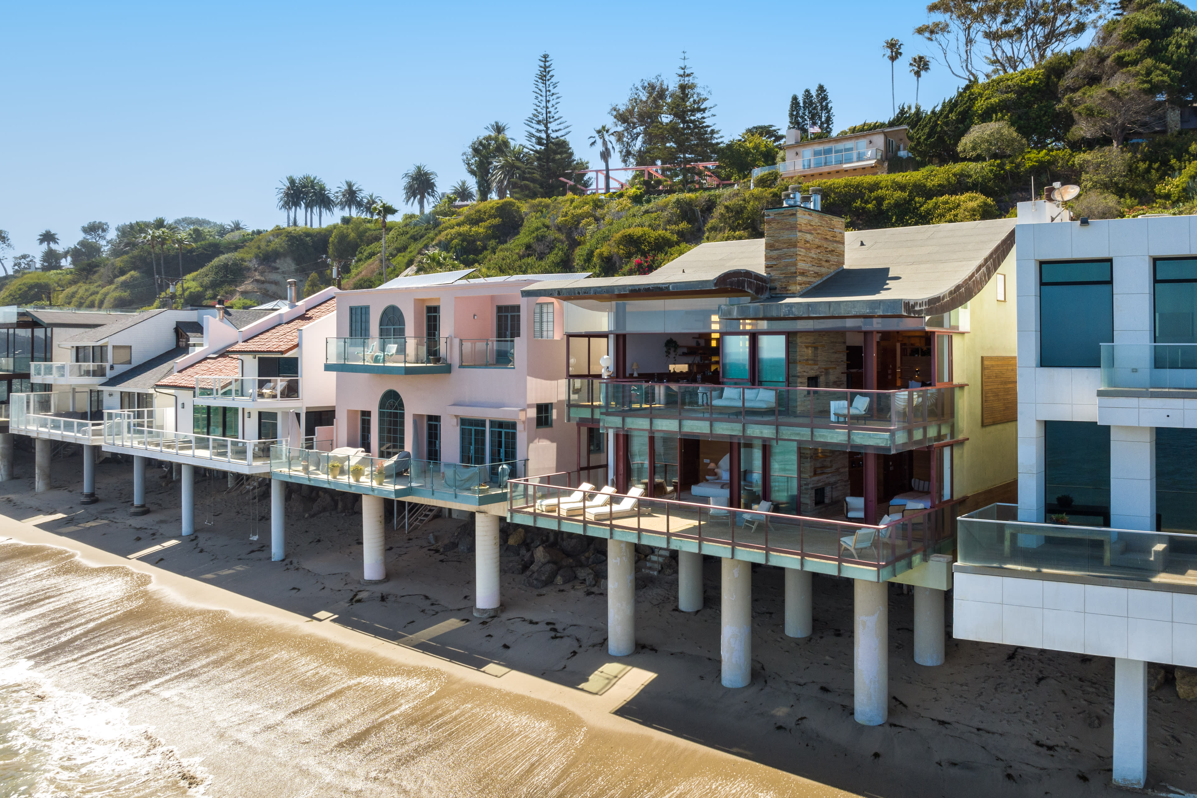 A row of modern beachfront homes with balconies elevated above the sandy shore.