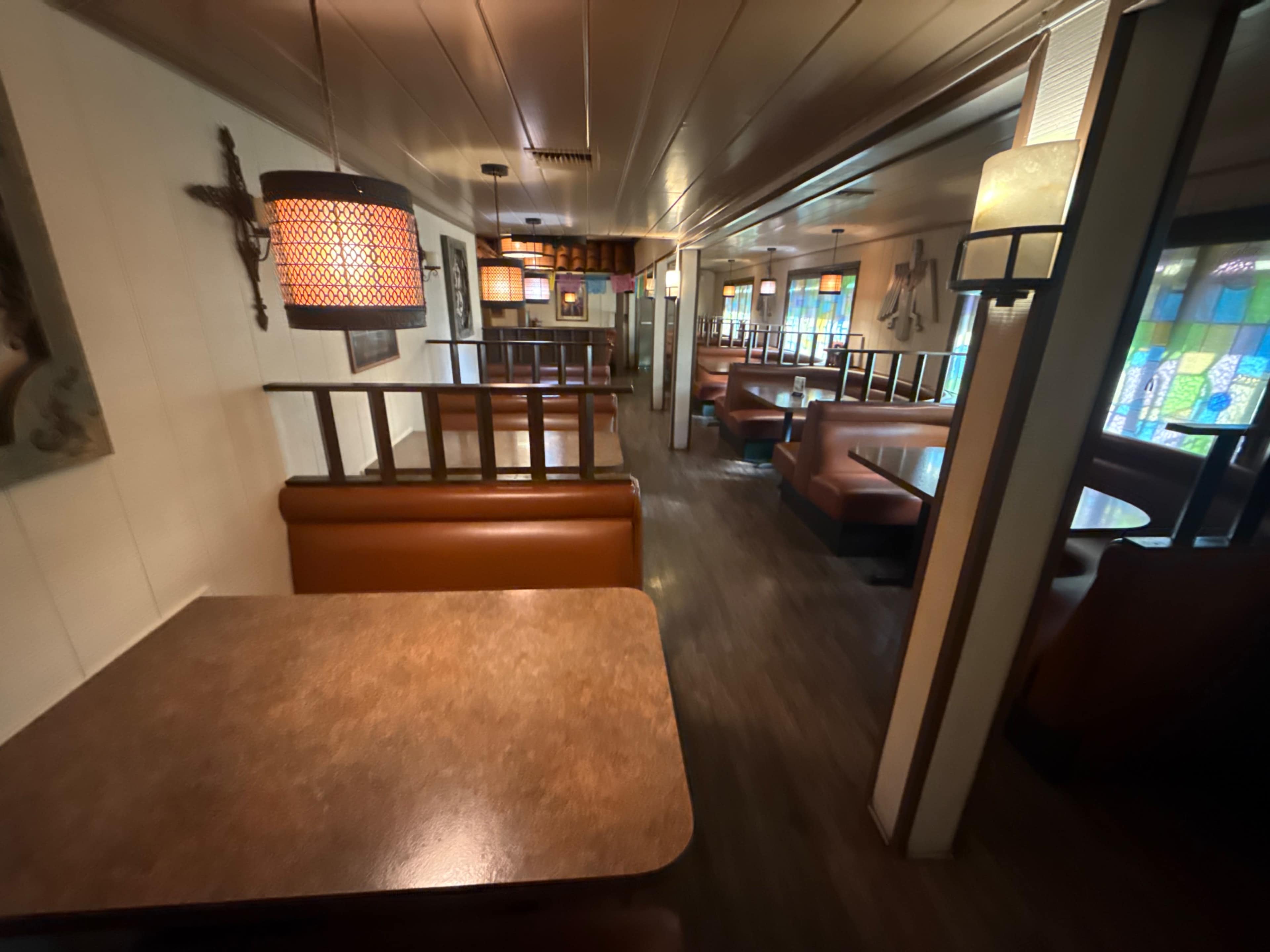 The image shows a spacious, warmly lit restaurant interior with brown booths and tables arranged along the walls.