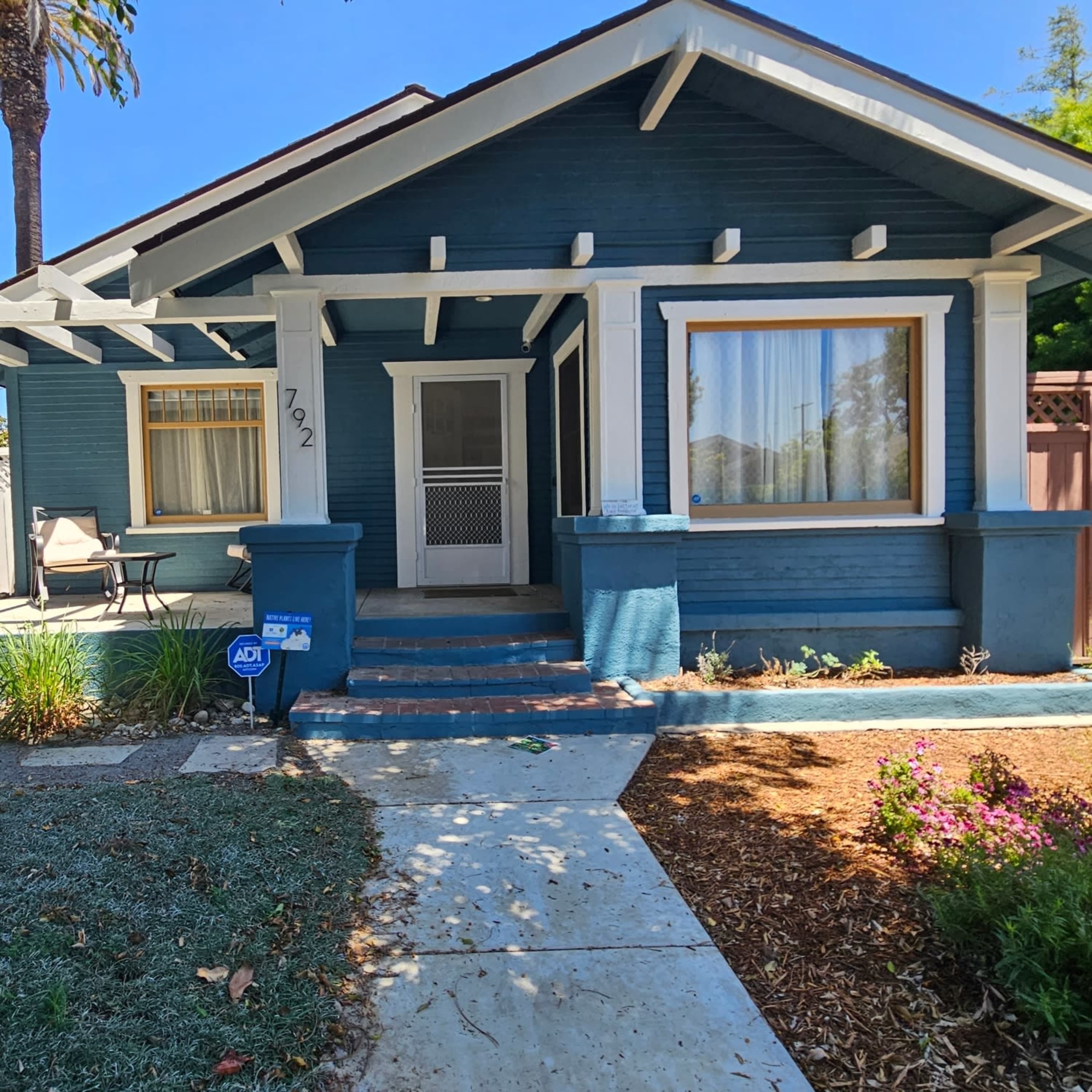 The image shows a blue, single-story bungalow with a front porch, white trim, and landscaped yard.