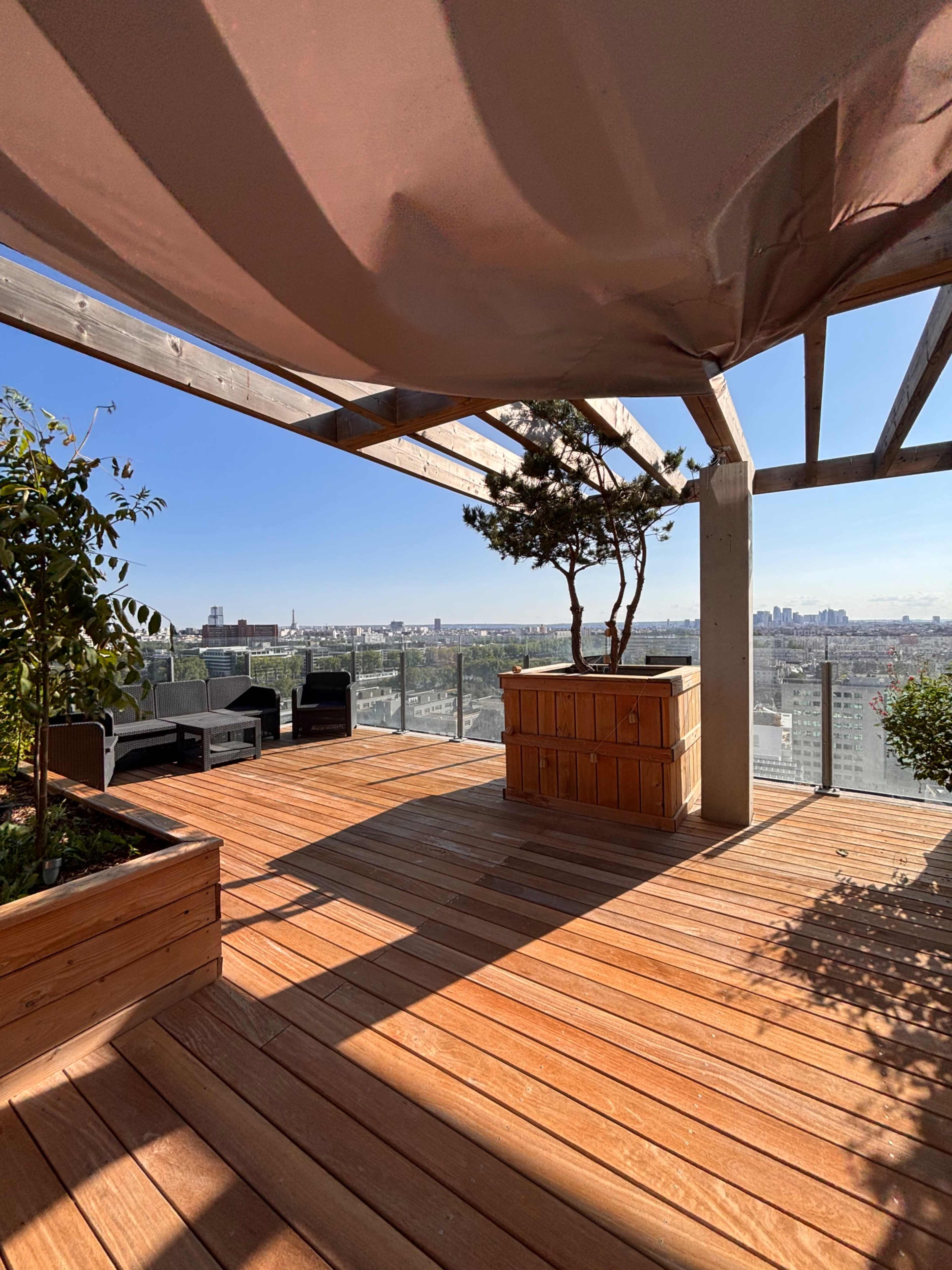 The rooftop terrace features wooden decking, a planter with greenery, and seating areas, all set against a backdrop of a city skyline.