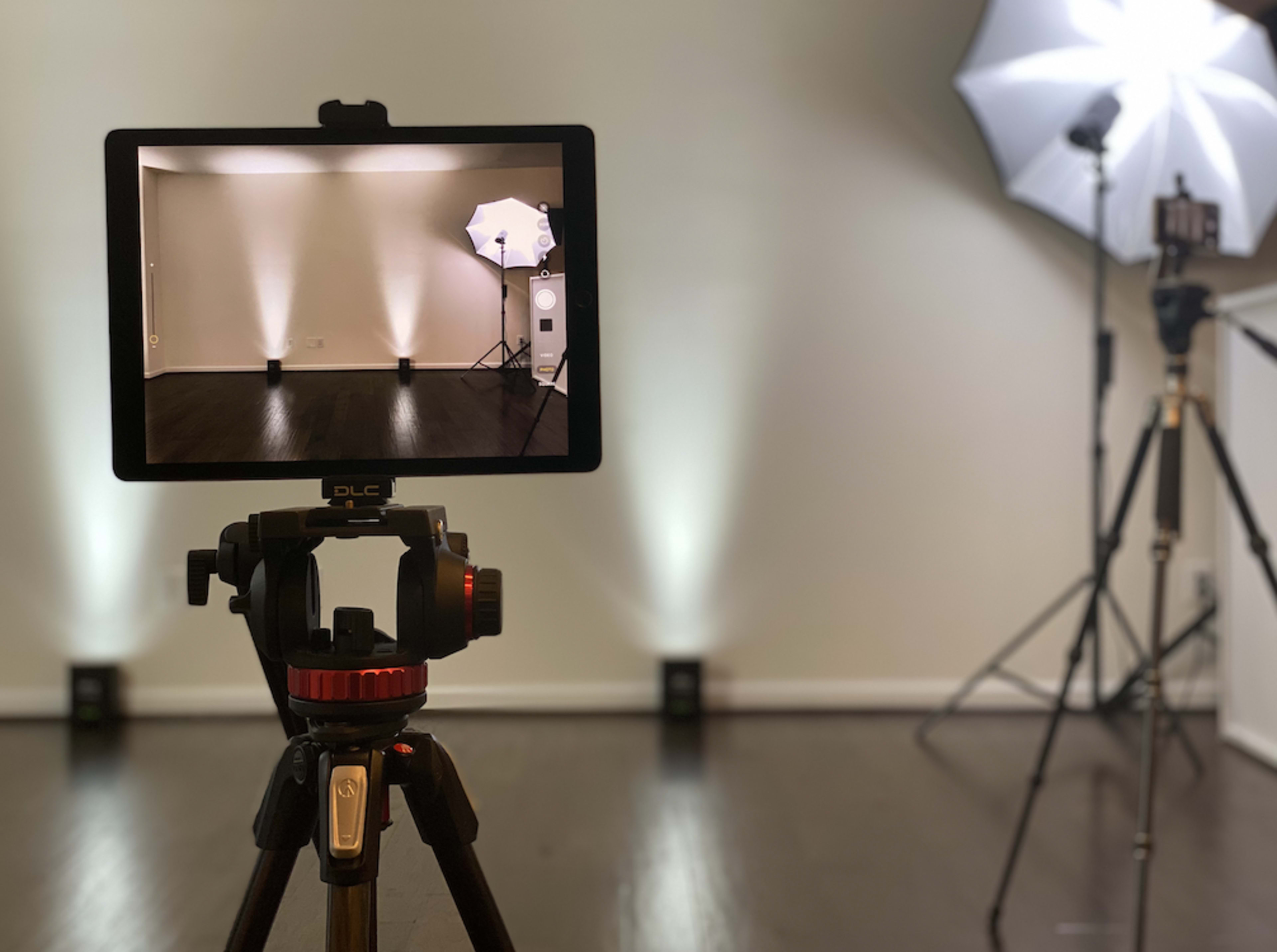 A camera mounted on a tripod is aimed at a studio setup with two softbox lights illuminating a minimalist room.