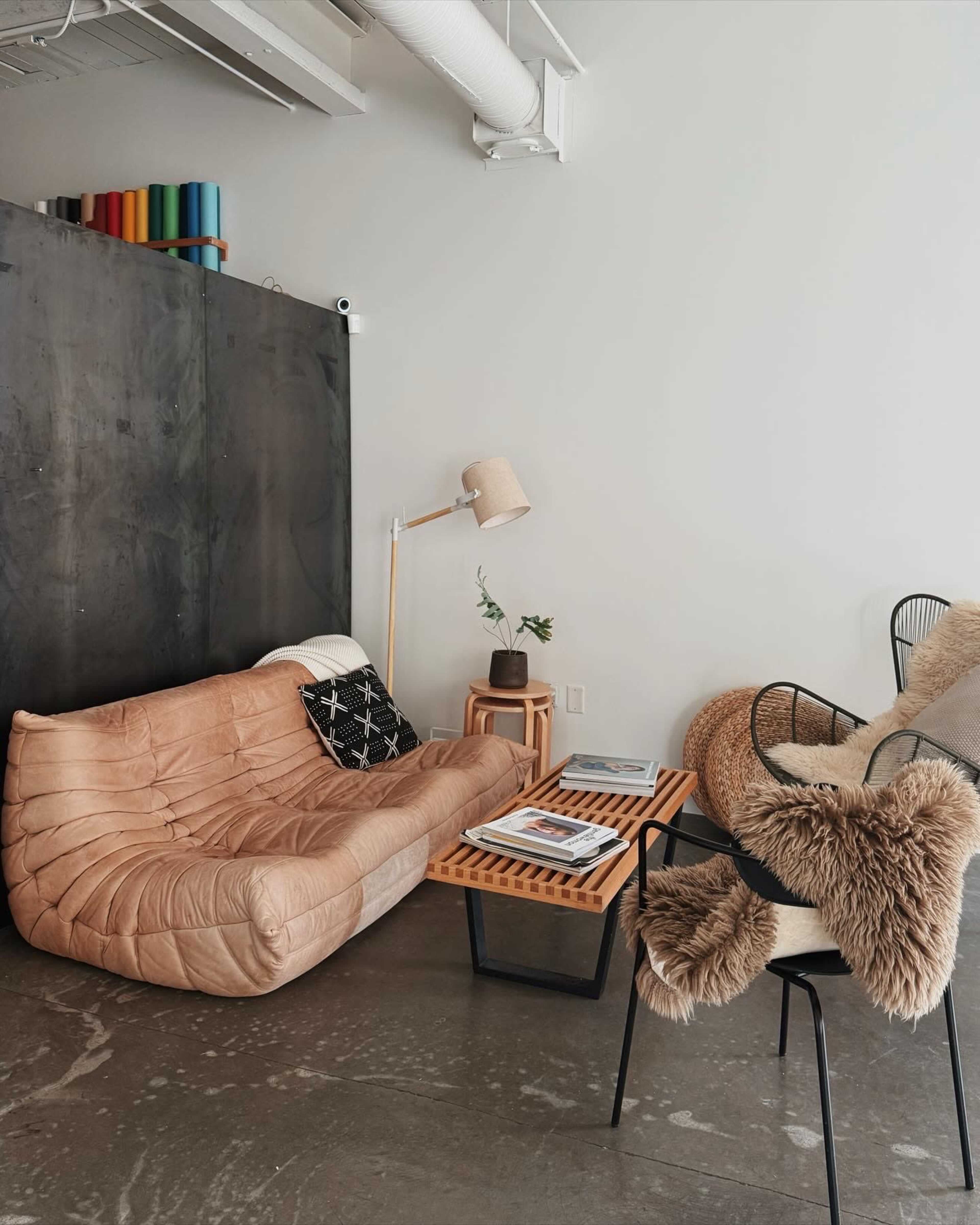 The image shows a modern living space featuring a tan leather sofa, a wooden coffee table, and a mix of chairs, with decor items arranged on the floor and walls.