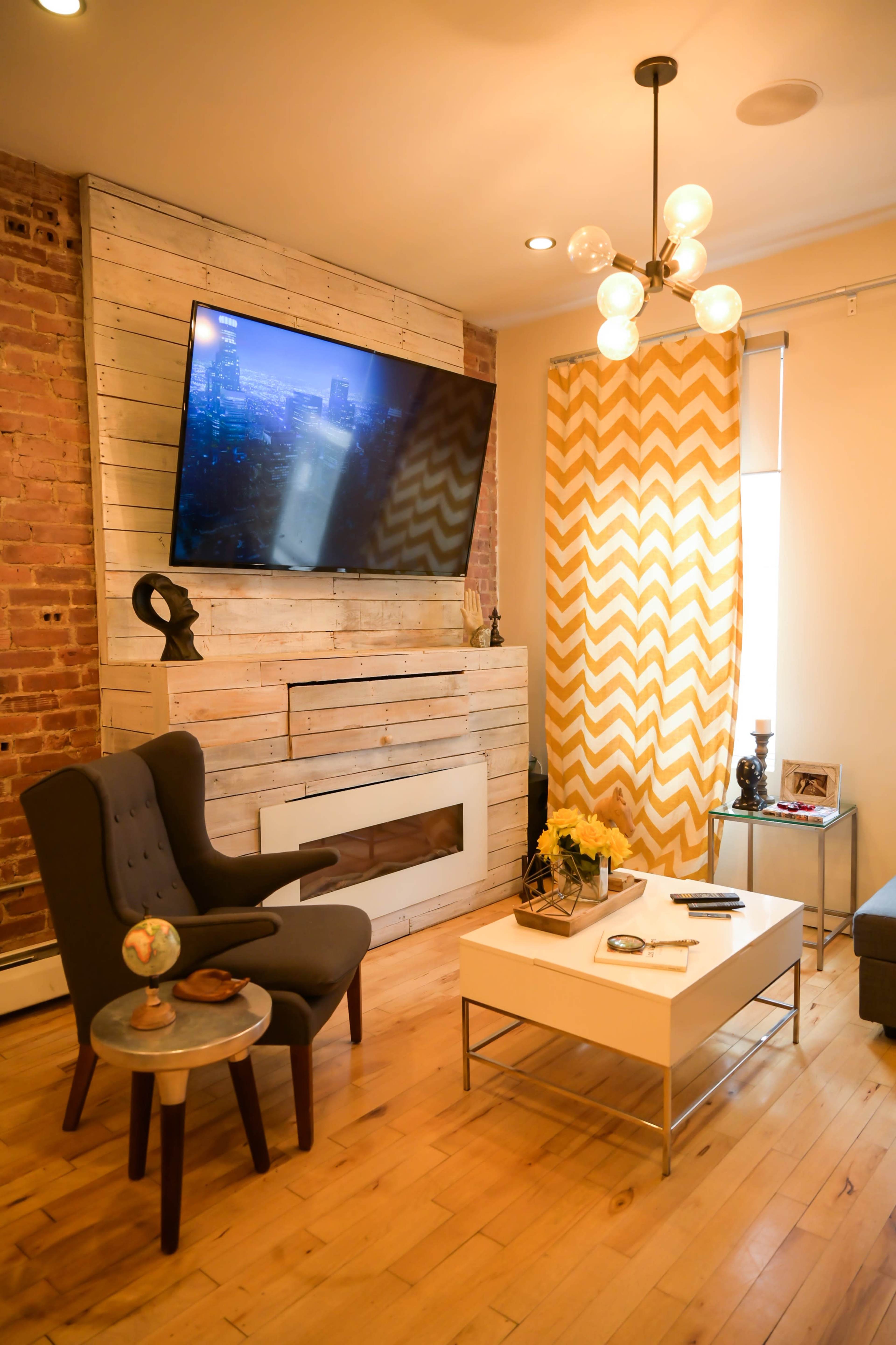 A modern living room features a large wall-mounted TV, a stylish chair, a coffee table, and a decorative curtain in a chevron pattern.