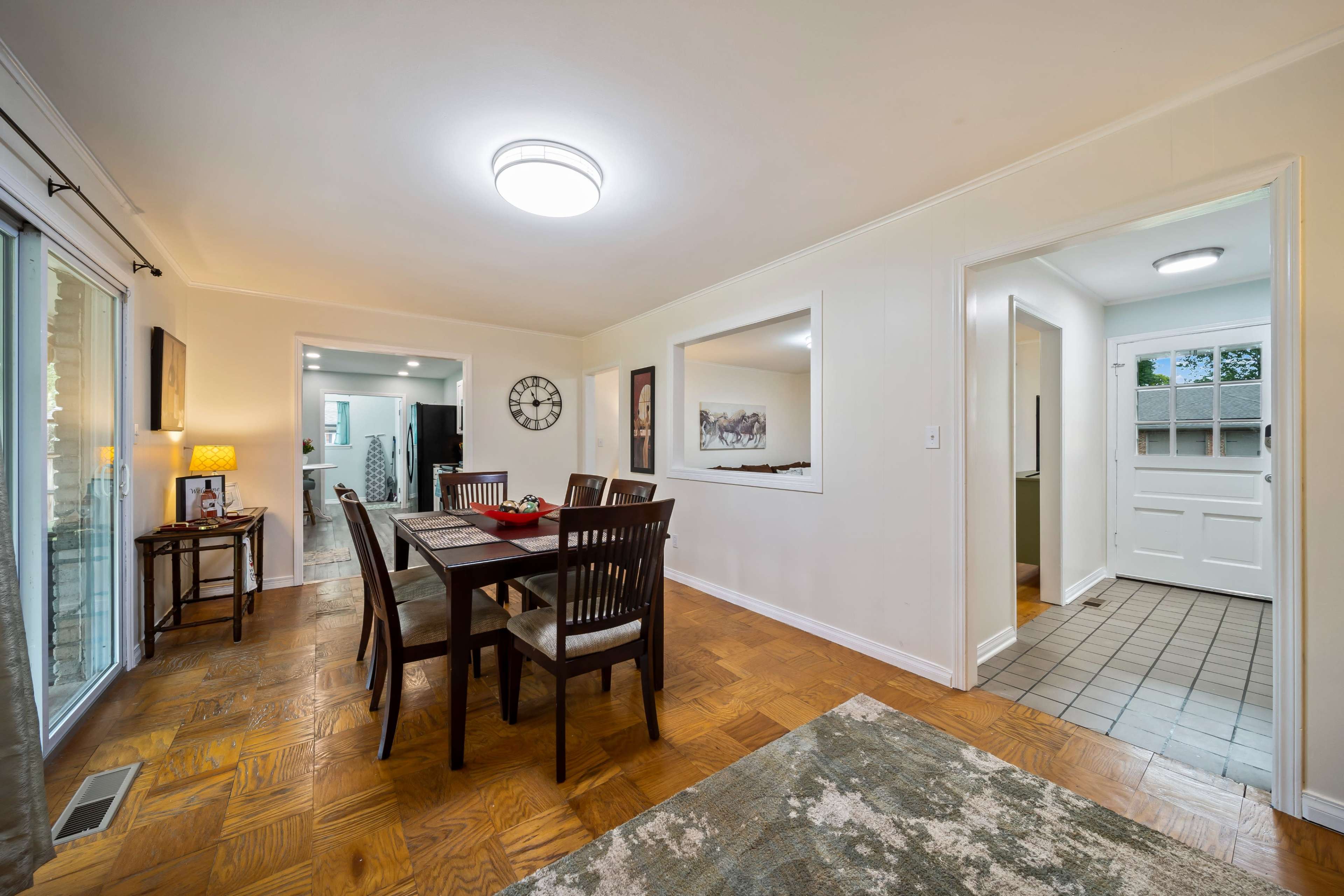 A dining area with a wooden table and chairs, open to a hallway leading to a bathroom and an exterior door.