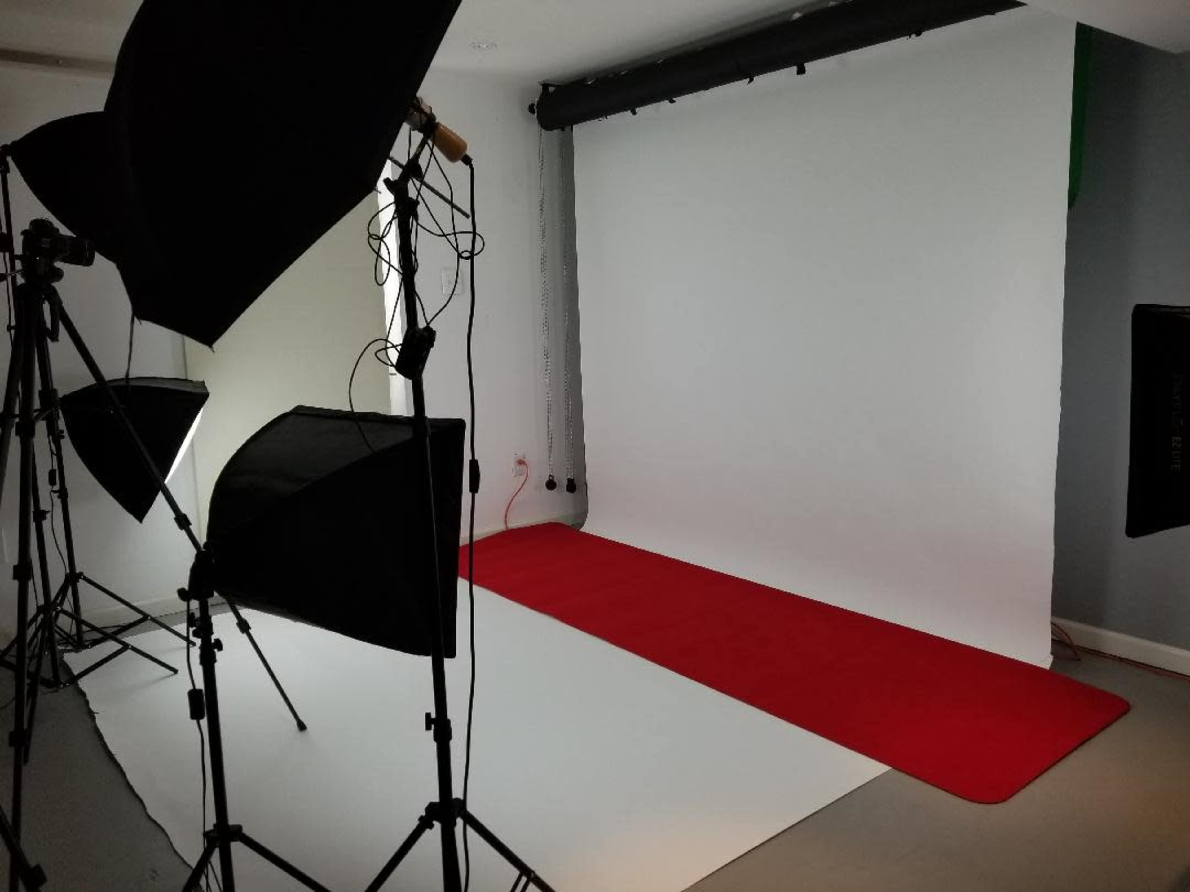 A photography studio with a red carpet, white backdrop, and several lighting setups on stands.
