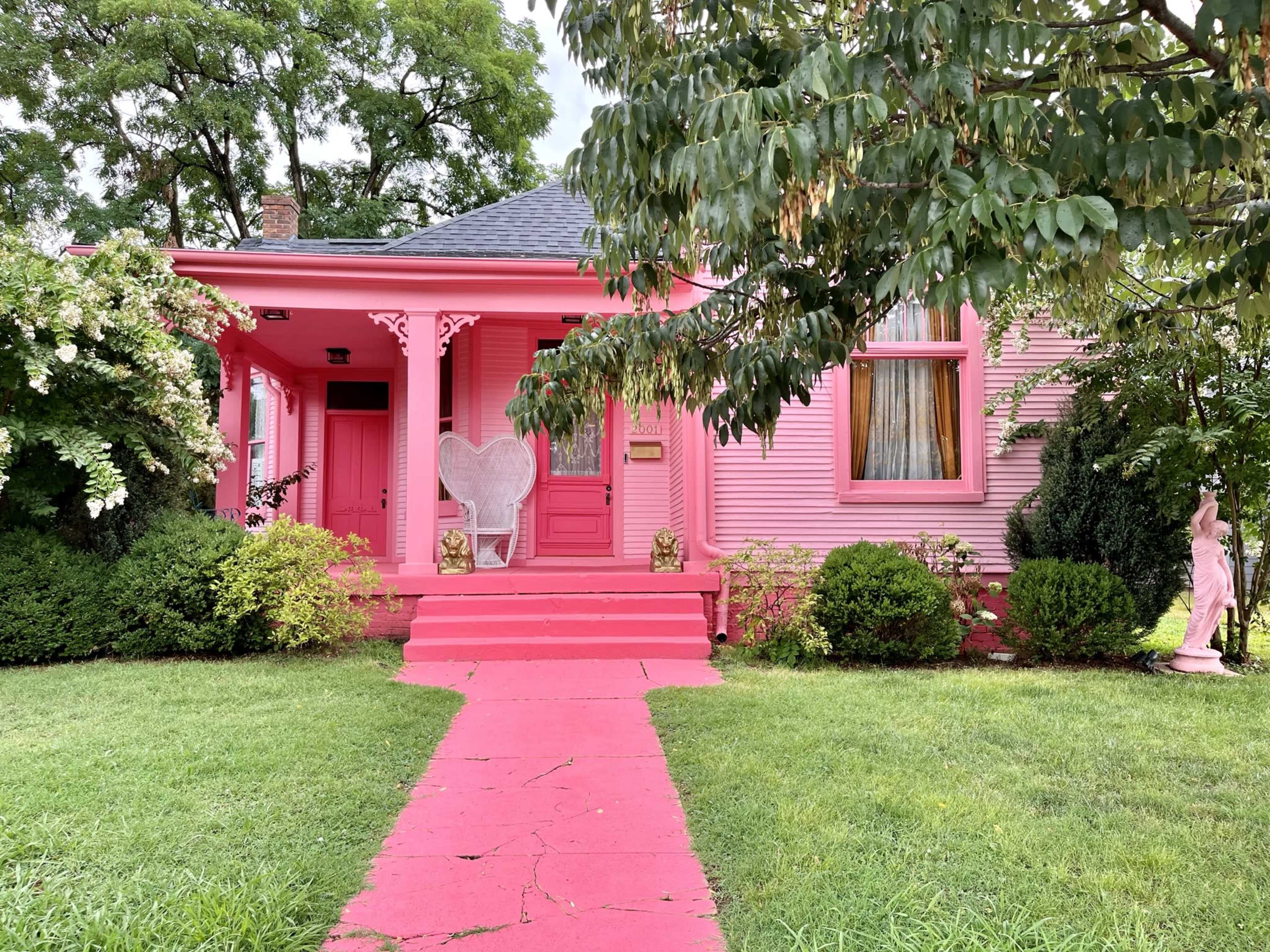 A pink house features a heart-shaped chair on the porch, with a bright pink pathway leading to it.