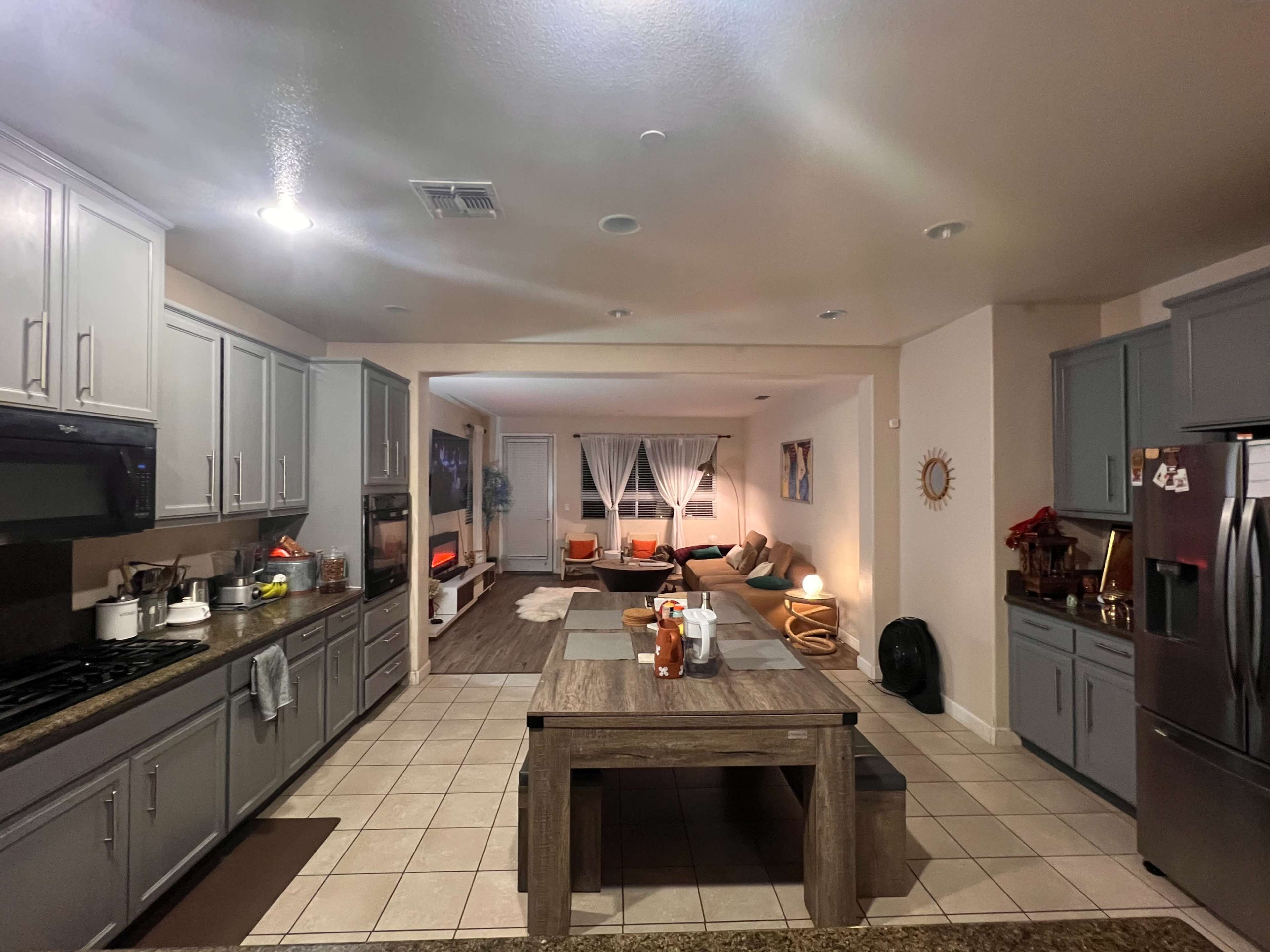A spacious kitchen with gray cabinets and countertops, leading into a living area furnished with a couch and a coffee table.