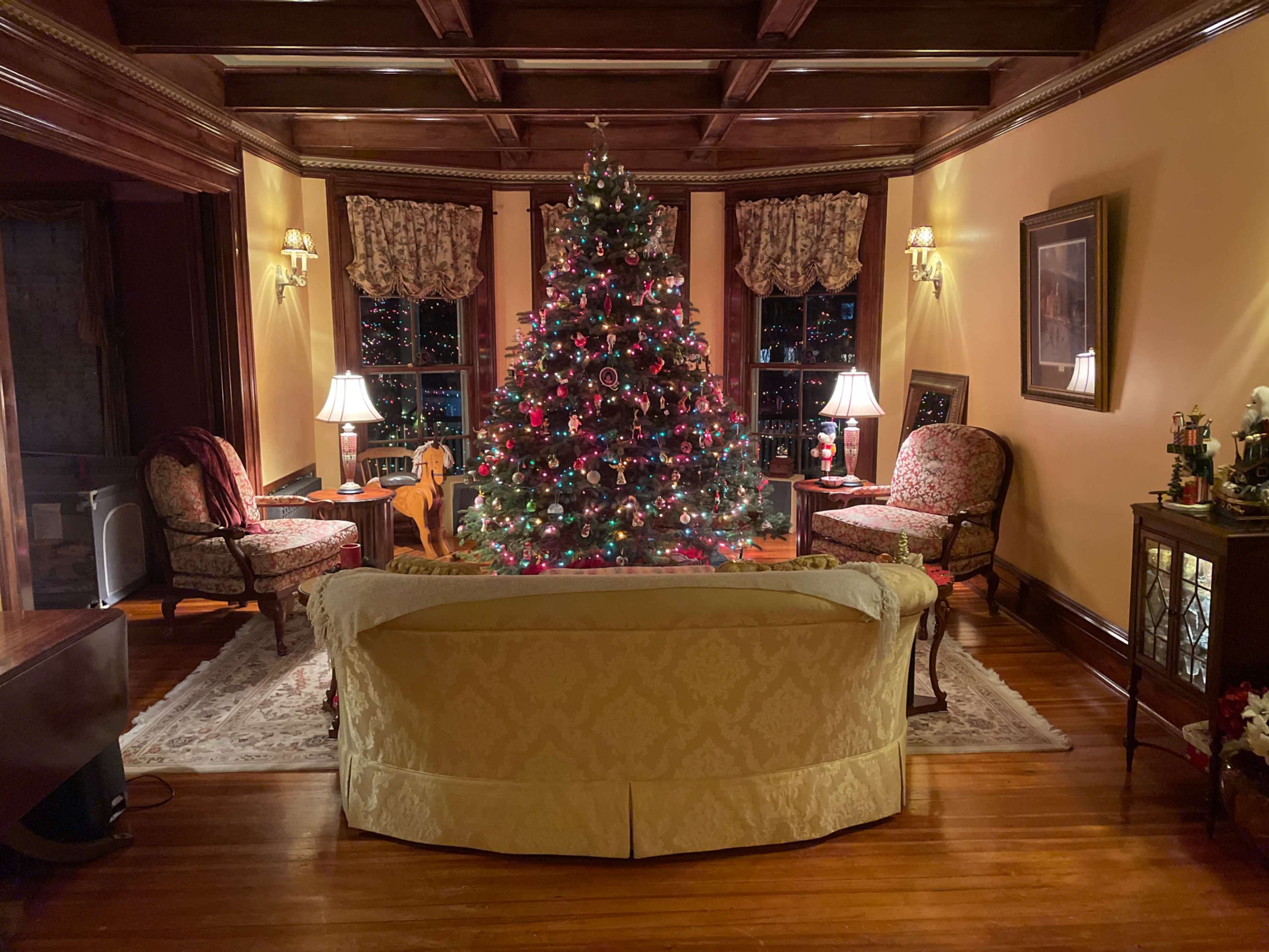 A cozy living room features a decorated Christmas tree surrounded by comfortable seating and softly lit lamps.