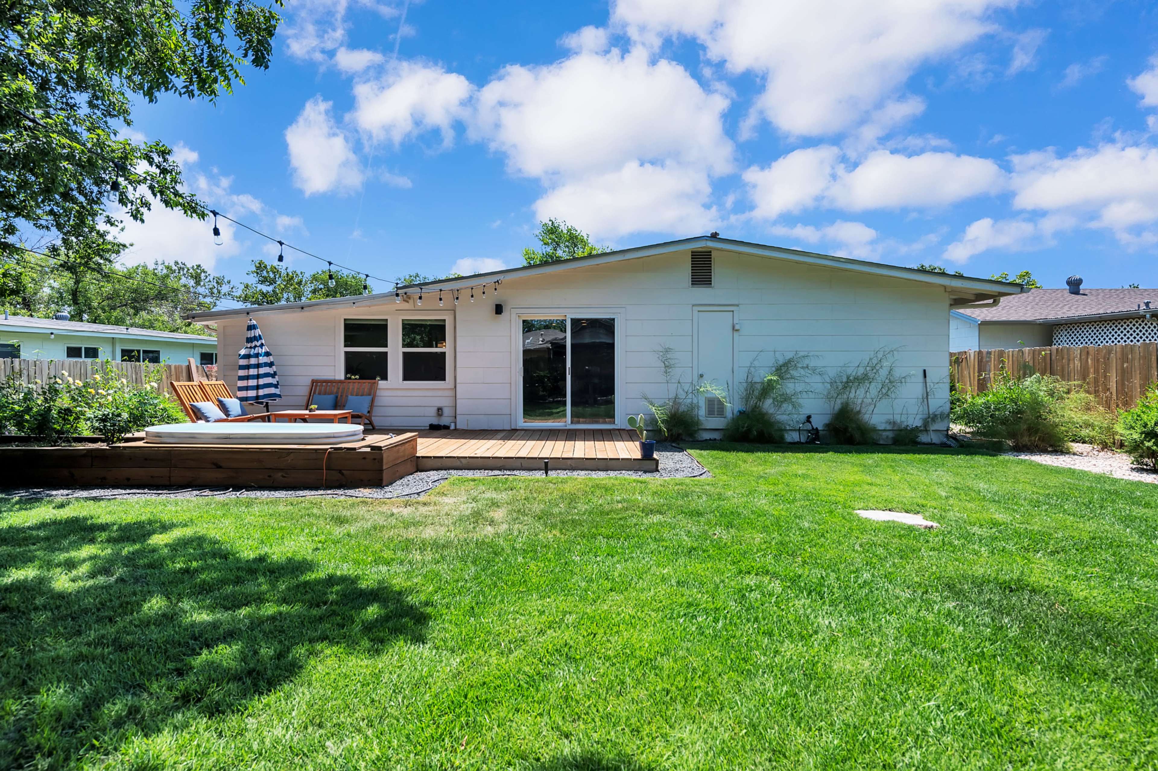 A modern single-story house with a wooden deck and landscaped backyard featuring a green lawn and patio furniture.