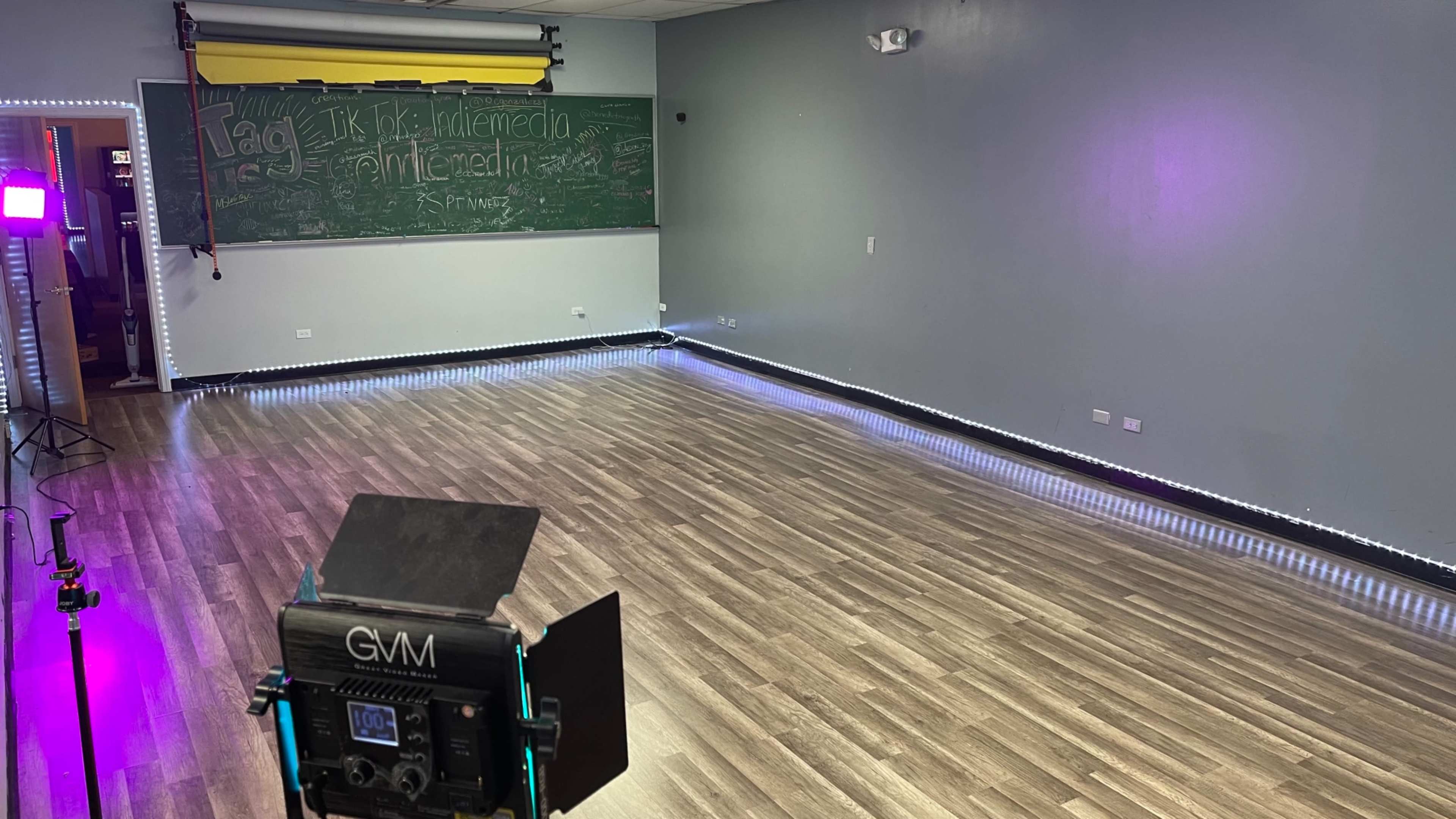 A sparsely decorated room features a chalkboard wall, a wooden floor, and LED strip lighting along the baseboards.