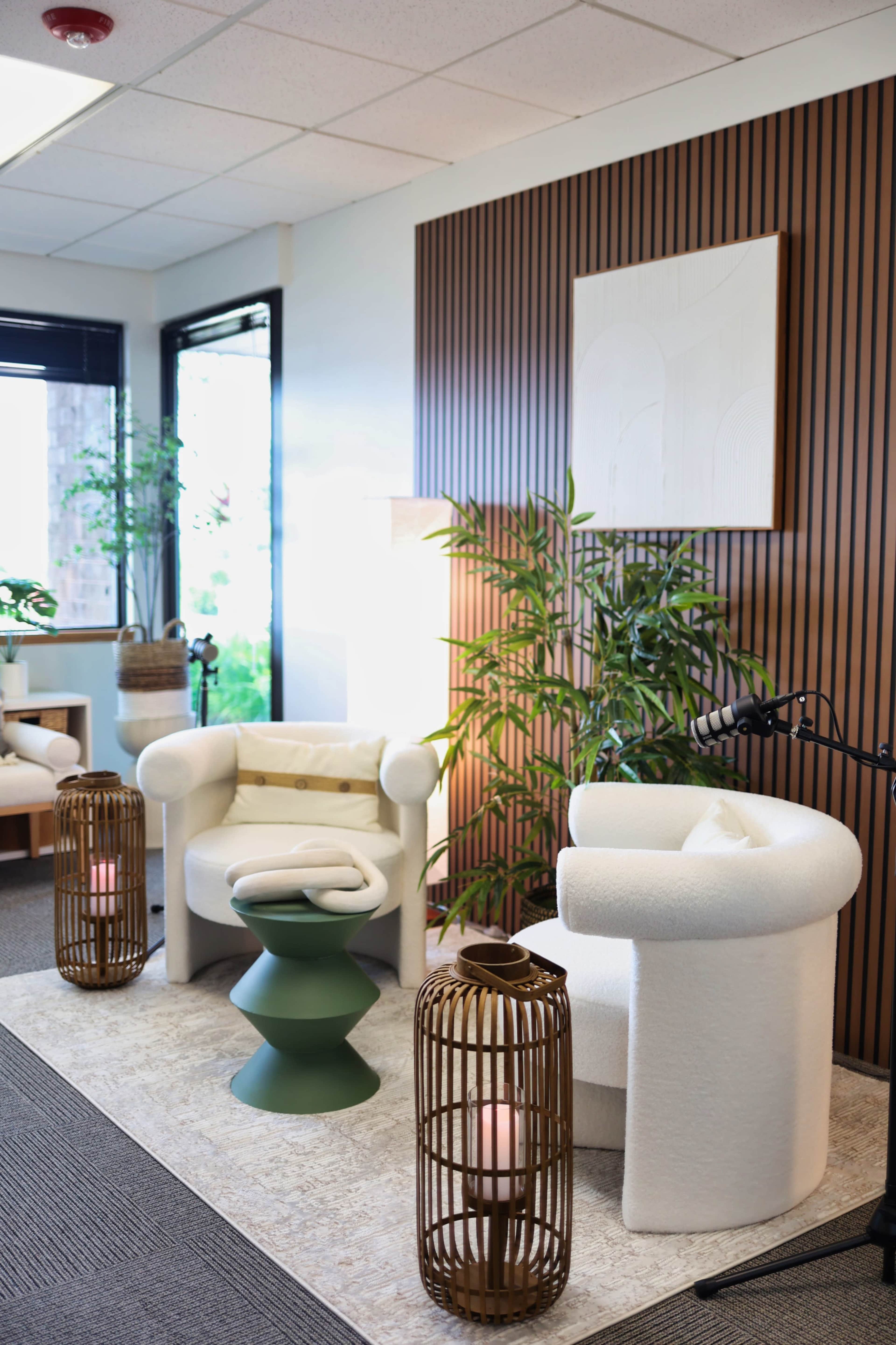 The image shows a modern interior space with two circular white armchairs, a green side table, and decorative plants, complemented by wooden panels and soft lighting.