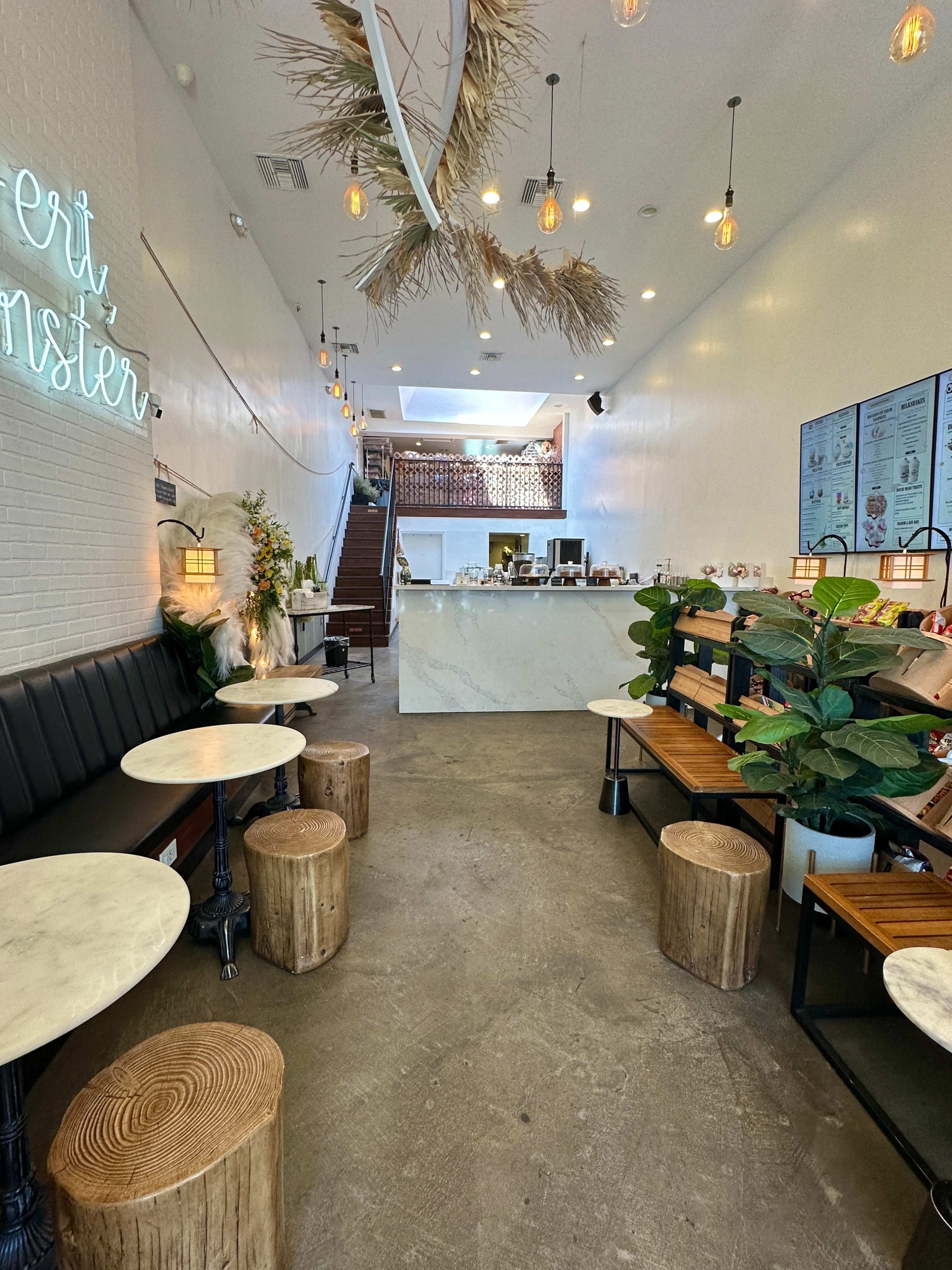 The interior of a modern café features wooden seating, marble counters, and decorative plants along a spacious layout.