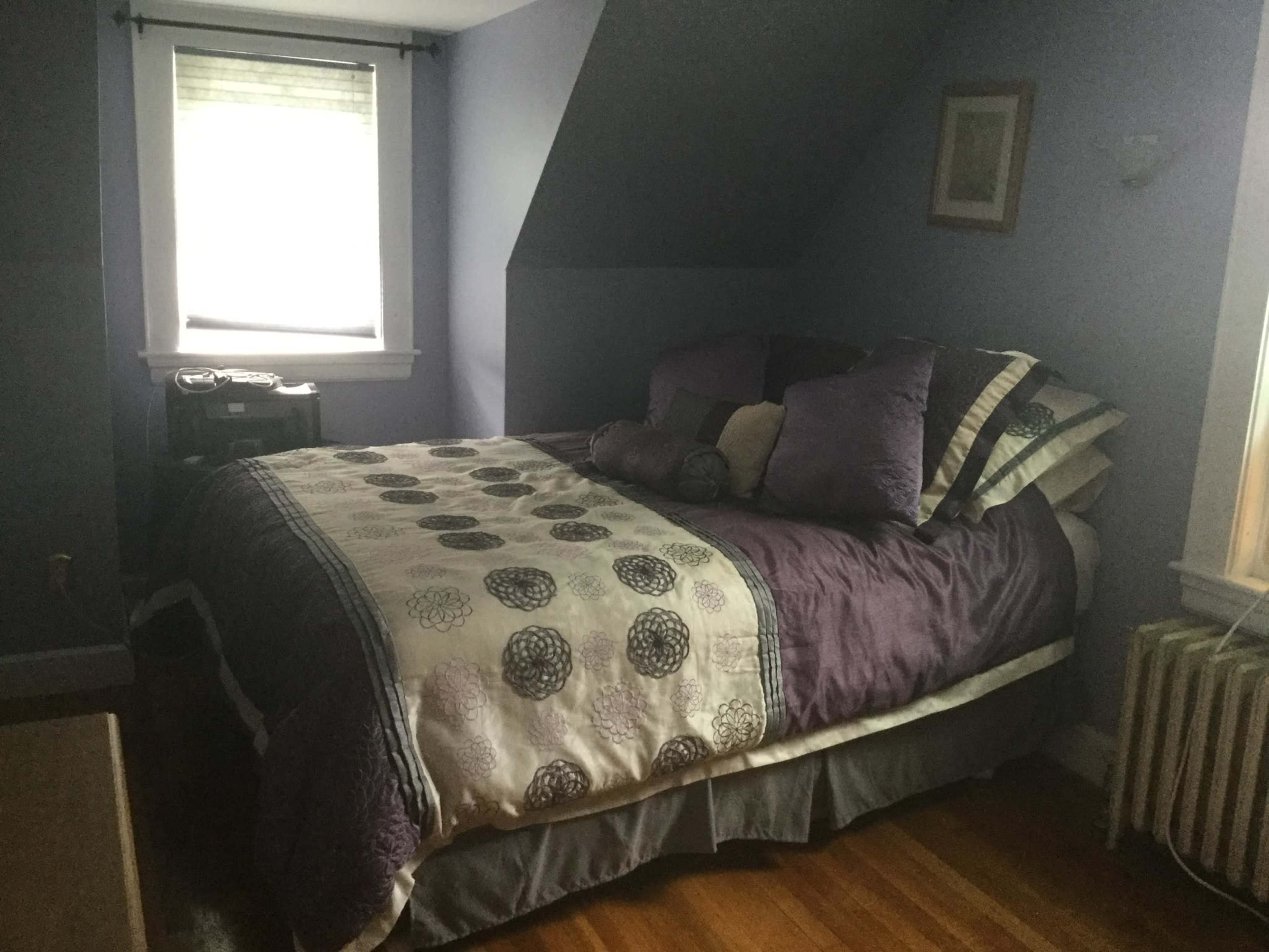 A cozy, slanted-roof bedroom with a bed covered in a decorative quilt and pillows, along with a window letting in natural light.
