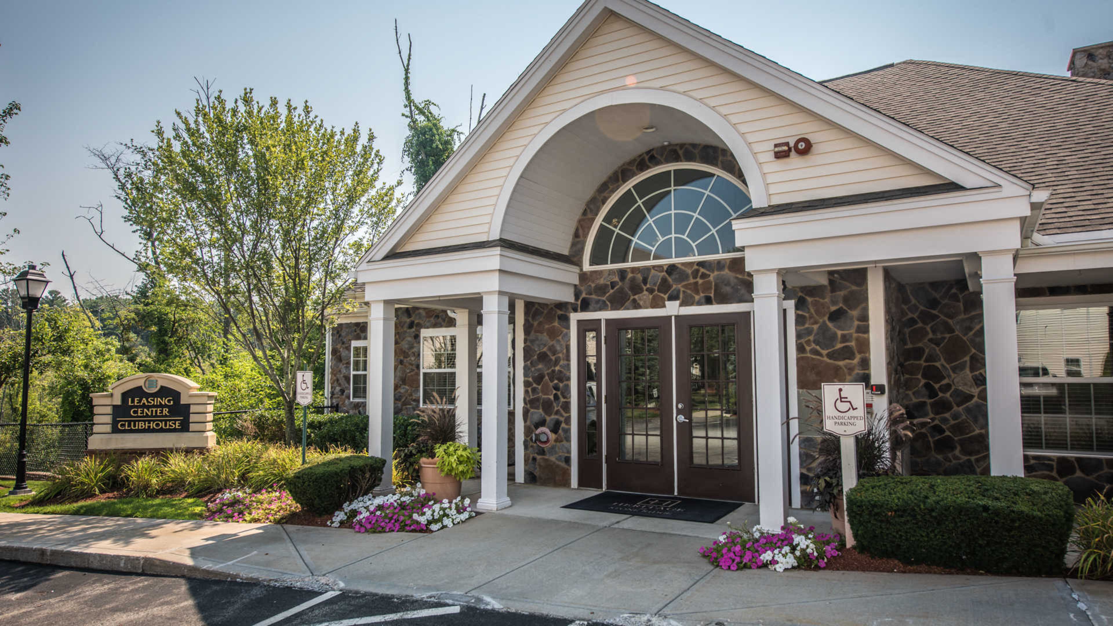 A leasing center clubhouse with a stone facade, large arched windows, and a landscaped entrance.