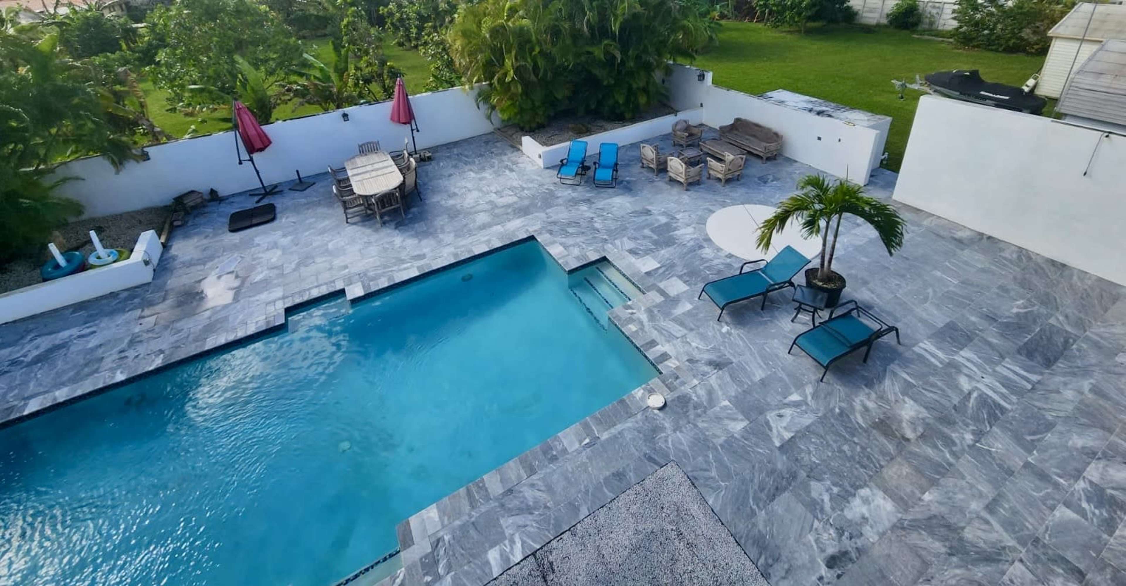 A landscaped outdoor area featuring a swimming pool, several lounge chairs, a dining table, and various plants.