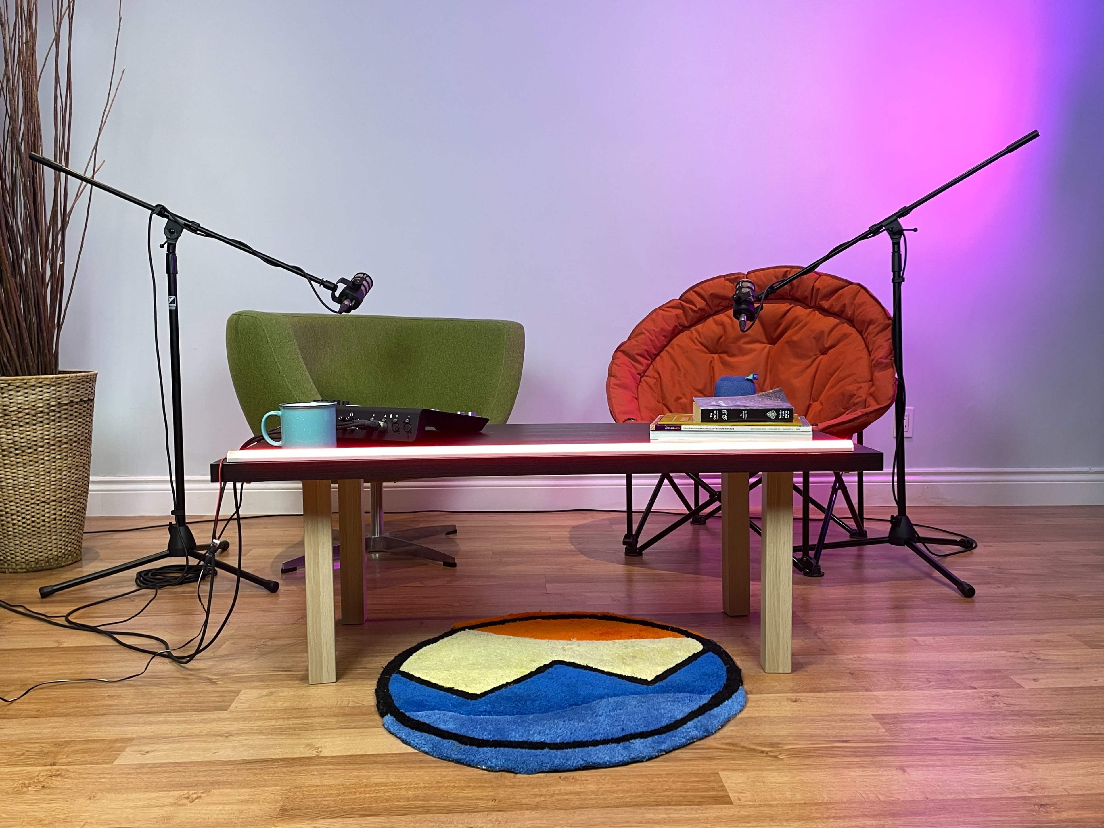 A small table with two chairs on either side, equipped with microphones, and a colorful rug on a wooden floor.