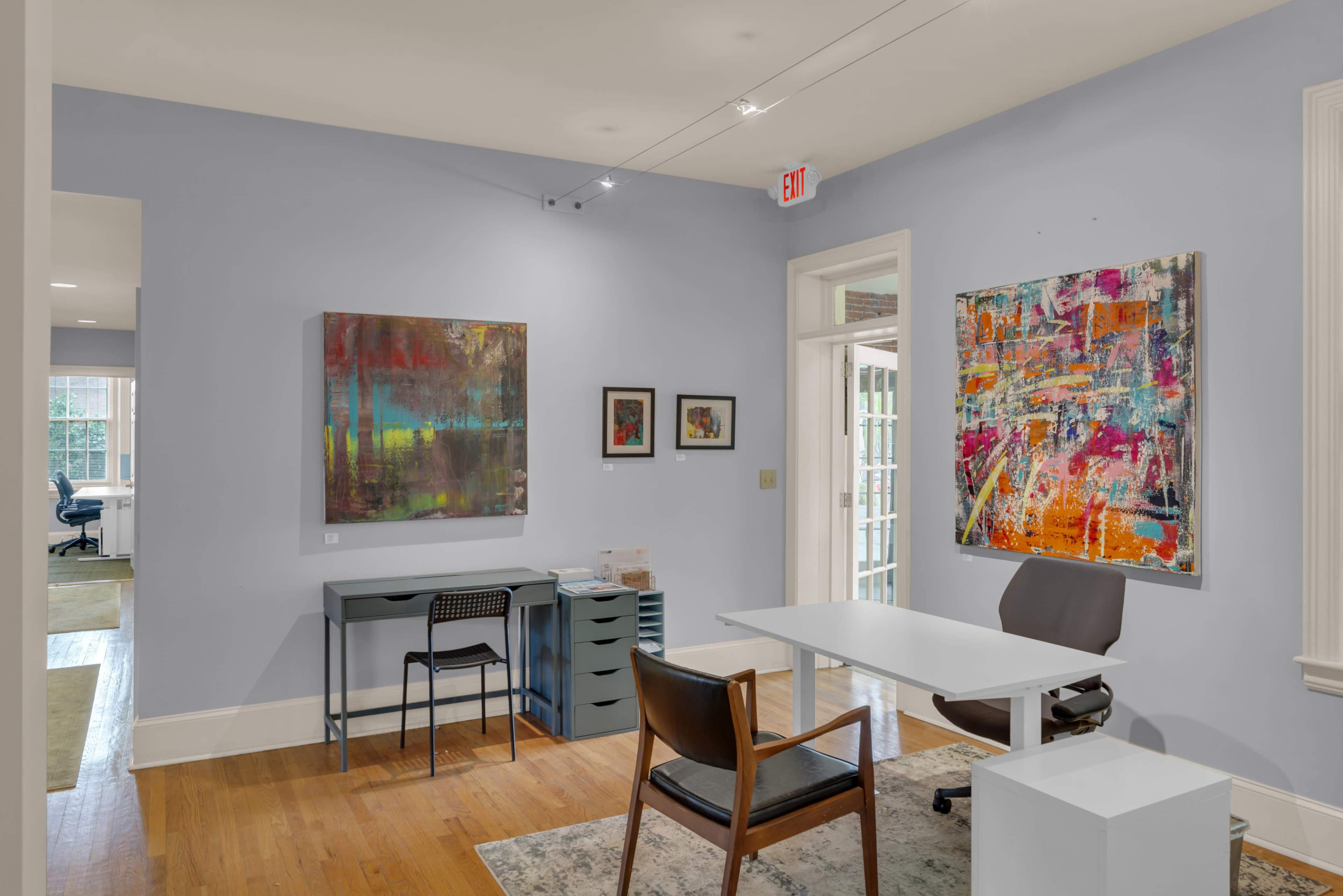 The image shows a modern office space with light blue walls, a desk, a chair, and colorful abstract artwork on the walls.