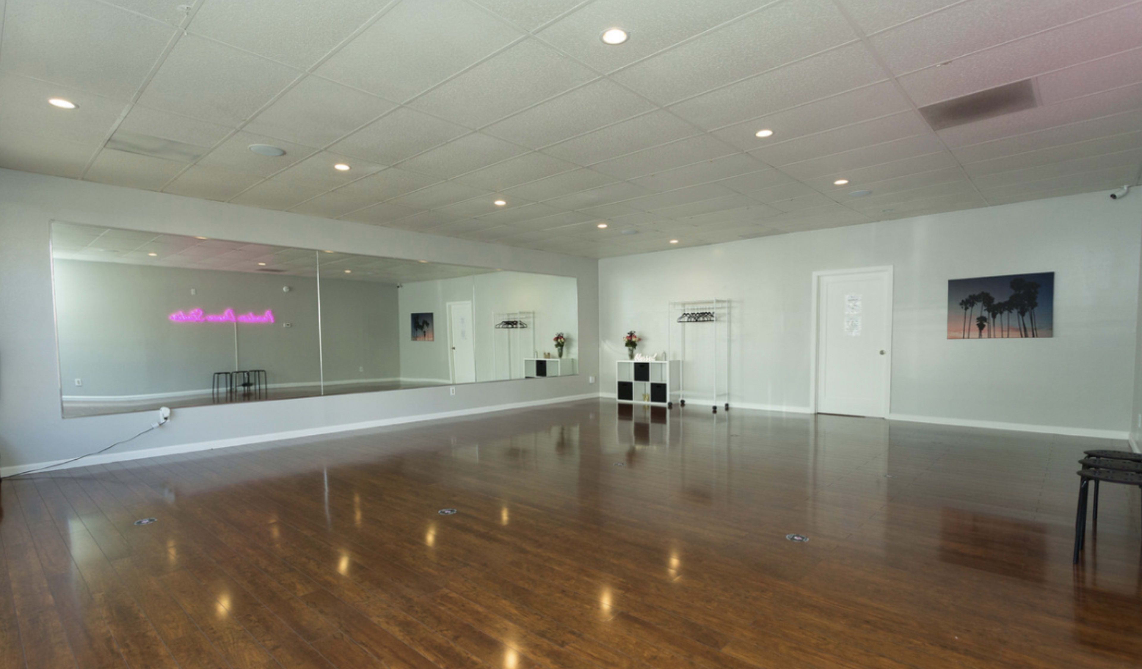 The image shows a spacious dance studio with mirrored walls, polished wooden floors, and minimal decorative elements.