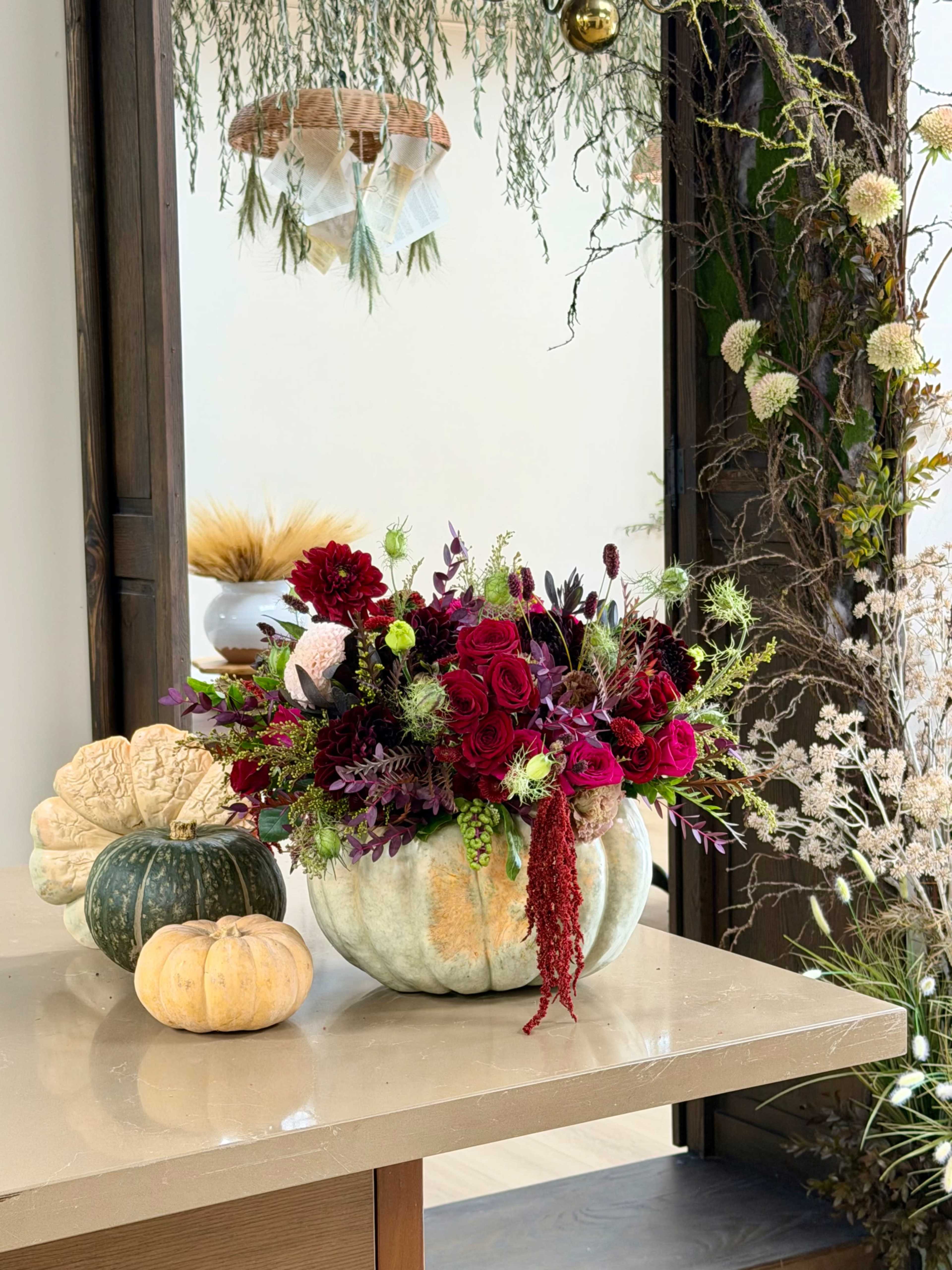A decorative arrangement of flowers in a pumpkin-shaped vase sits on a table alongside two smaller pumpkins.