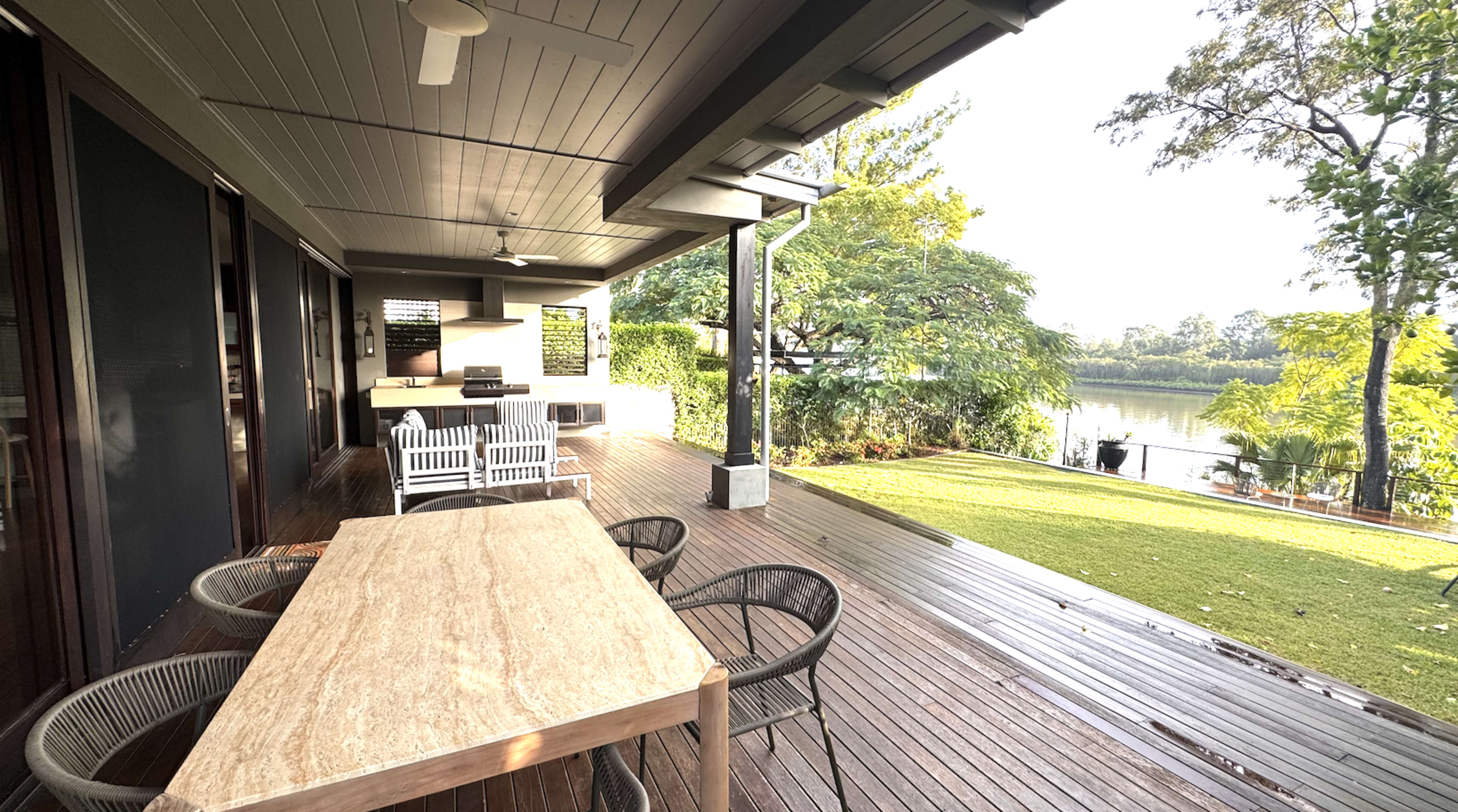 A wooden deck with a dining table and chairs overlooks a serene body of water surrounded by greenery.