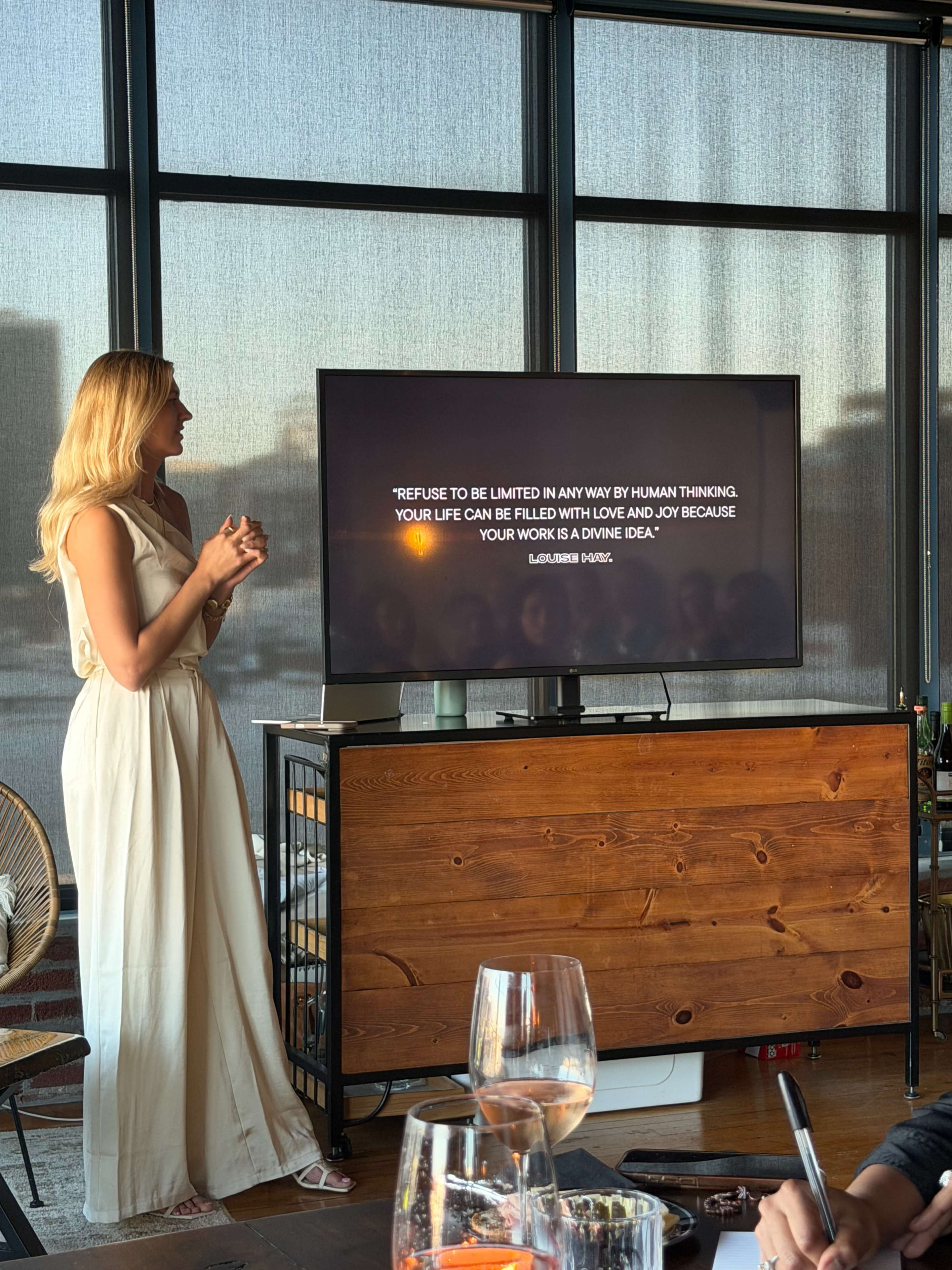 A woman in a white dress stands beside a television displaying a motivational quote in a modern indoor setting.