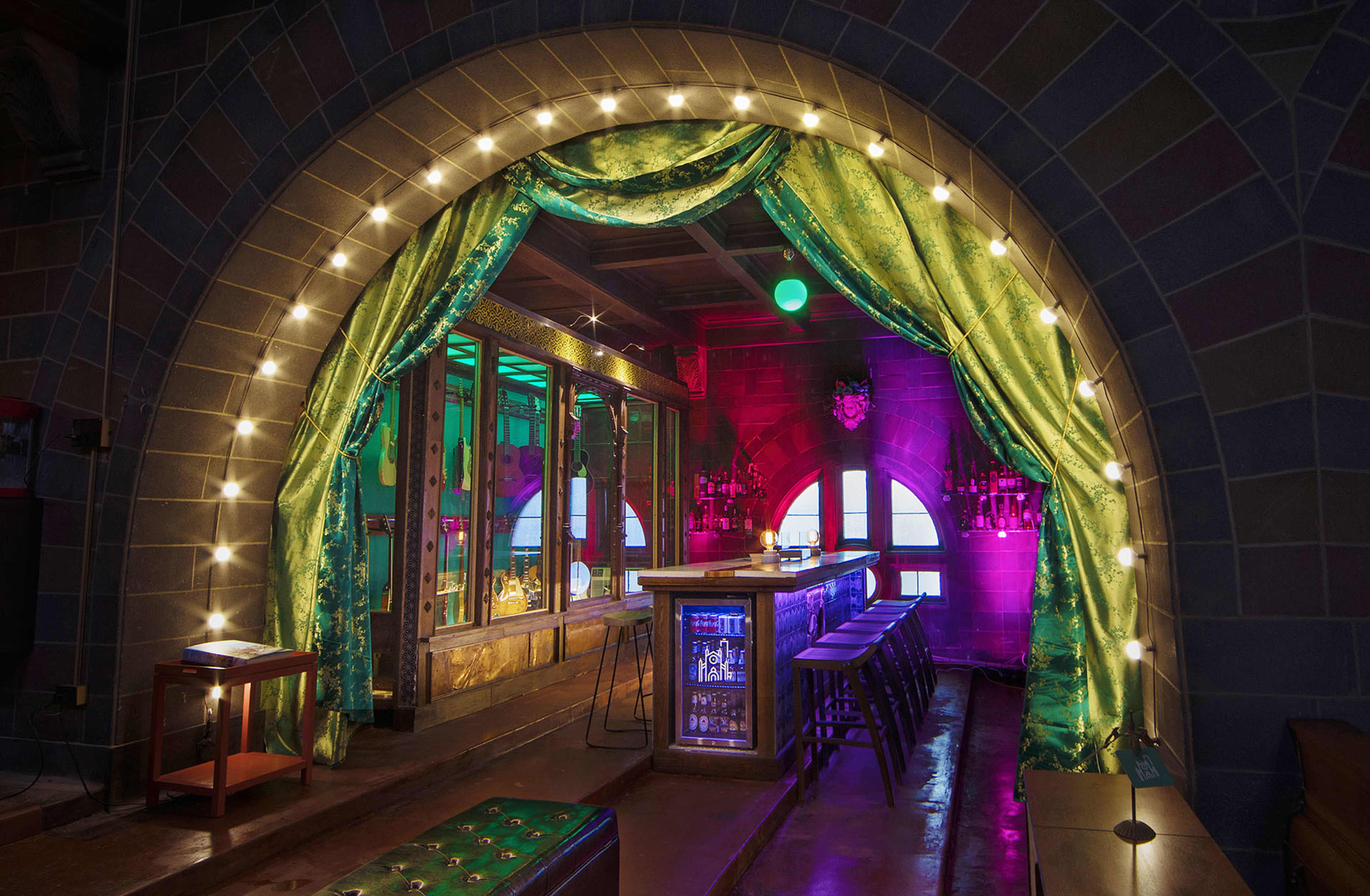 The image shows a brightly lit bar area with a decorative archway draped in green curtains and illuminated by string lights.