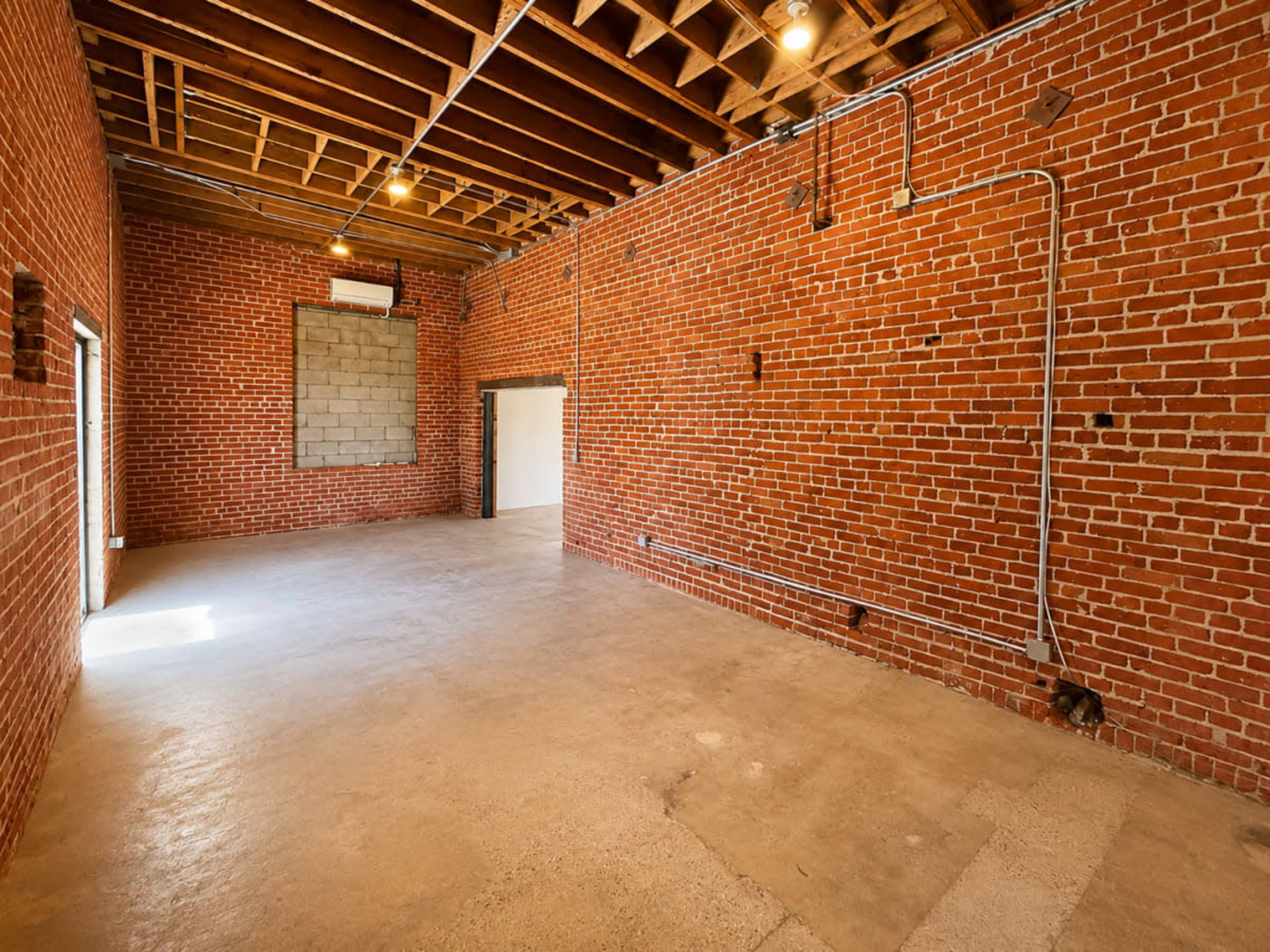 The image shows an empty industrial space with exposed brick walls and a concrete floor.