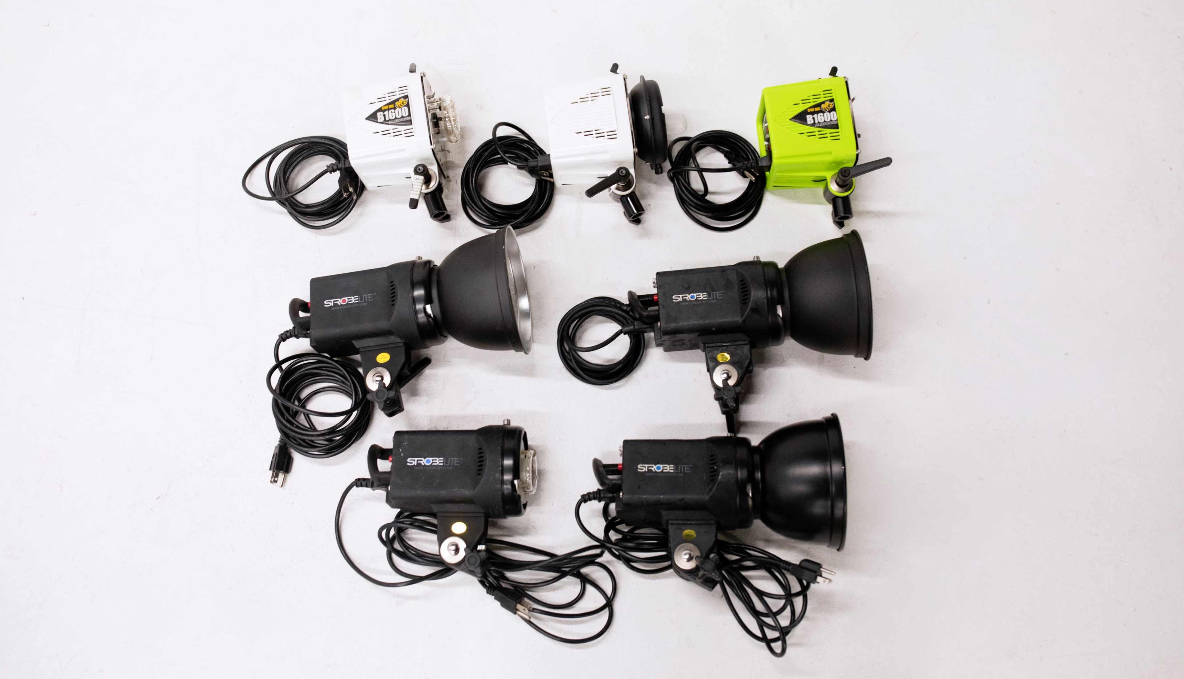 The image shows a layout of multiple lighting fixtures, including three black lights with reflectors and several small white and green control units, all connected by cables on a white surface.