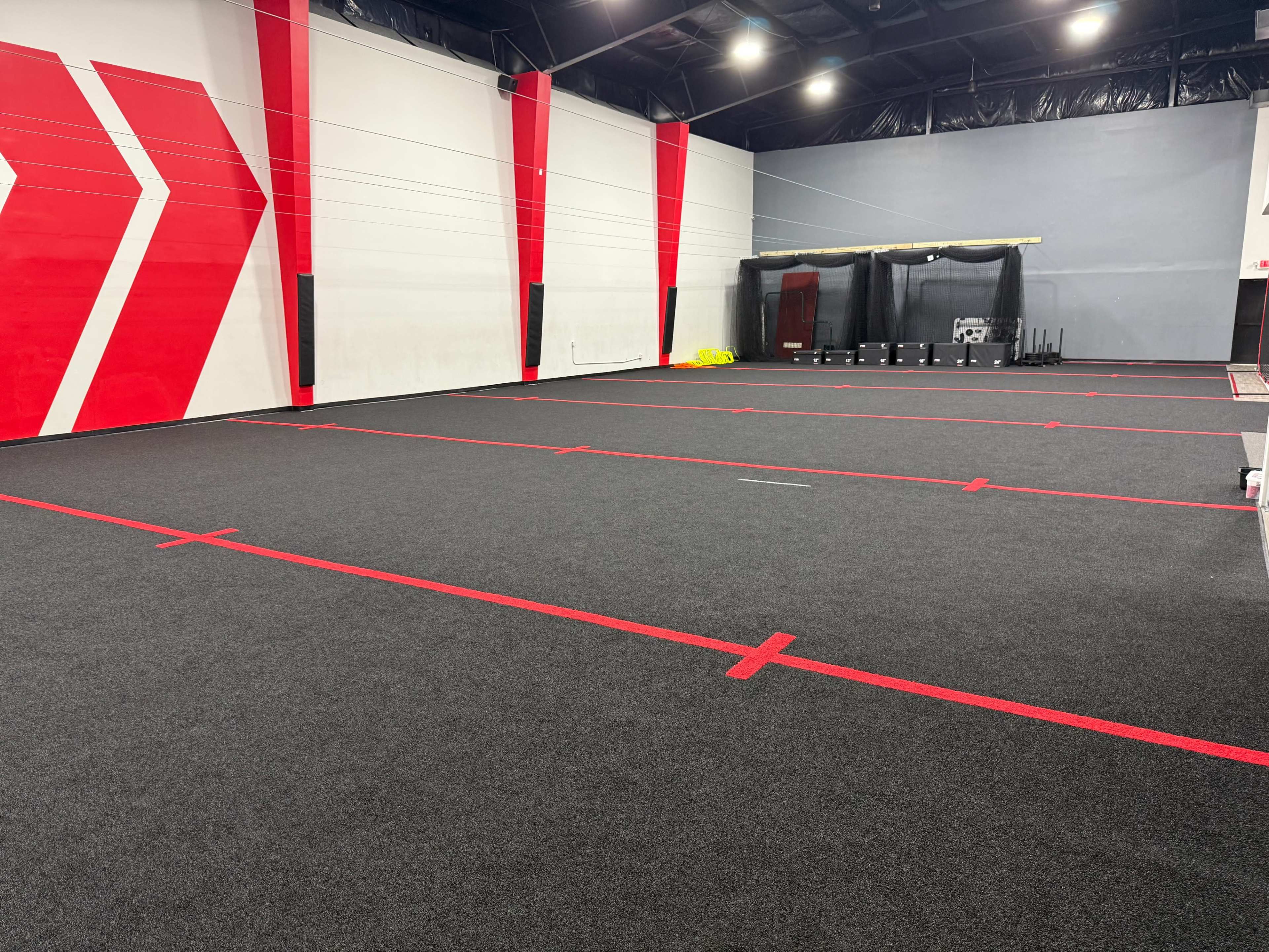 The image shows an indoor sports facility with a large black carpeted area, marked by red lines and contrasting red wall accents.