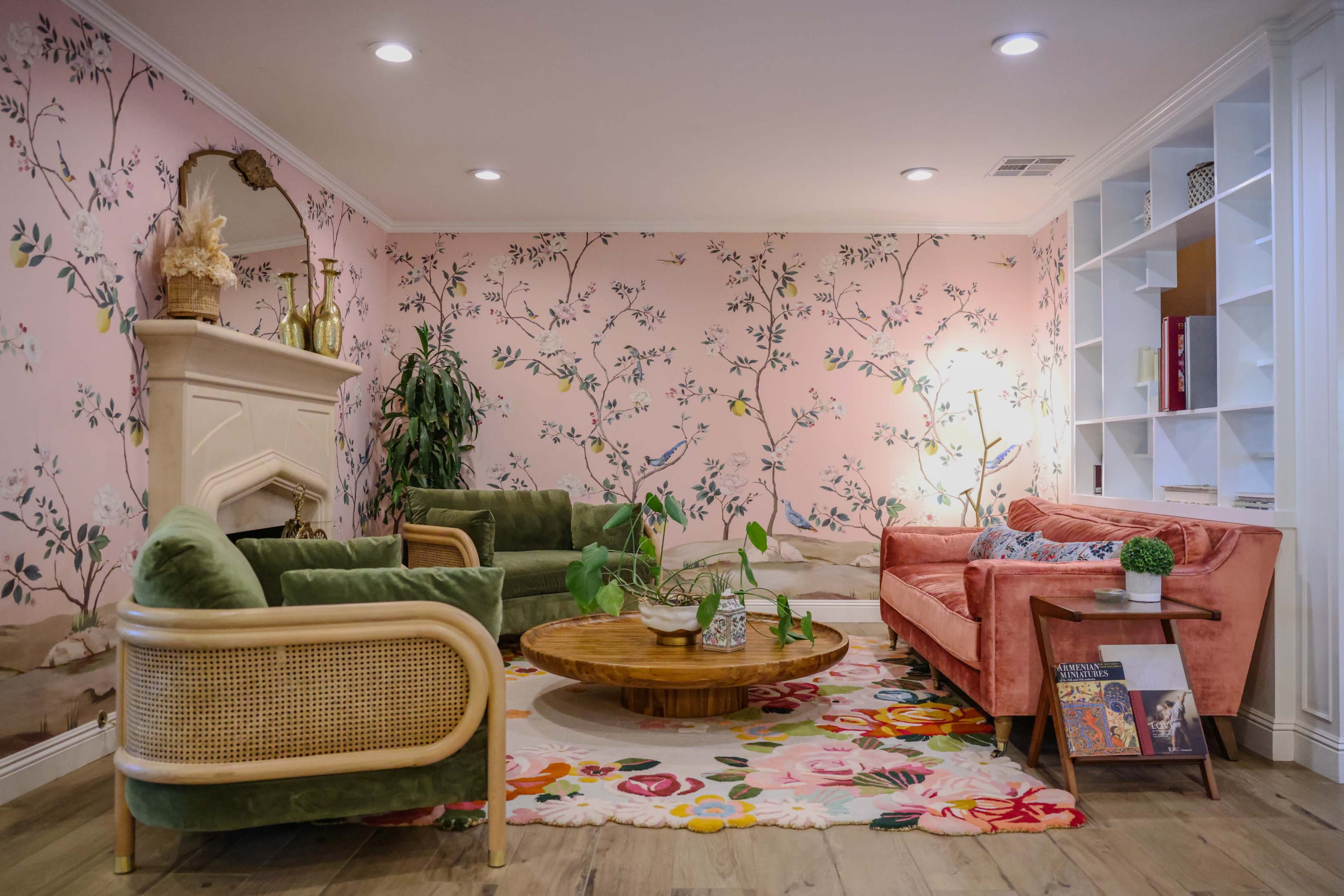 The image features a stylish living room adorned with floral wallpaper, green and pink furniture, and a circular wooden coffee table on a colorful area rug.
