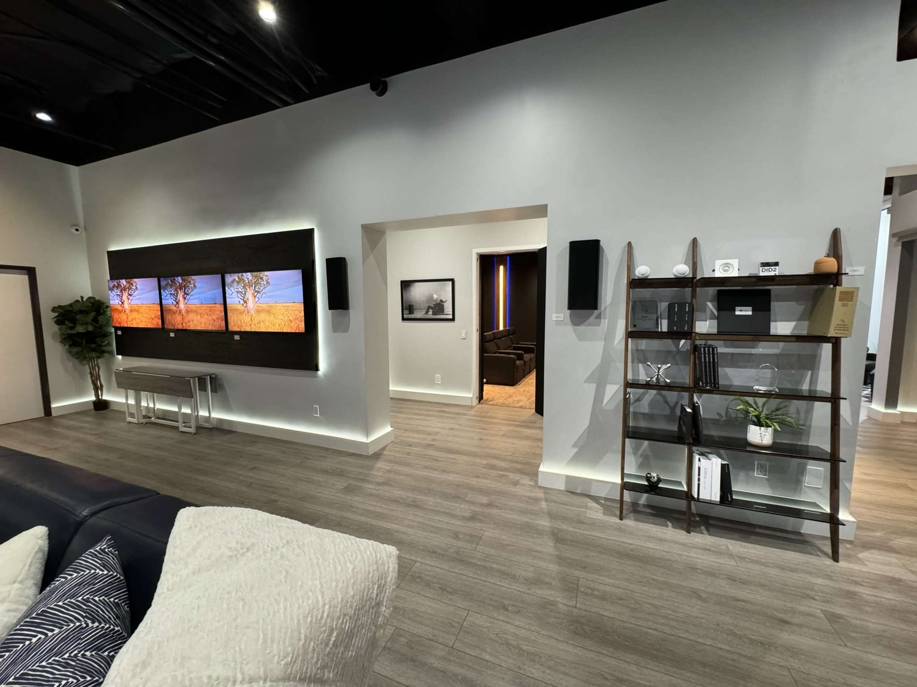 A spacious interior with a modern design featuring a large wall-mounted screen displaying a landscape, a shelf with decorative items, and an open doorway leading to another room.