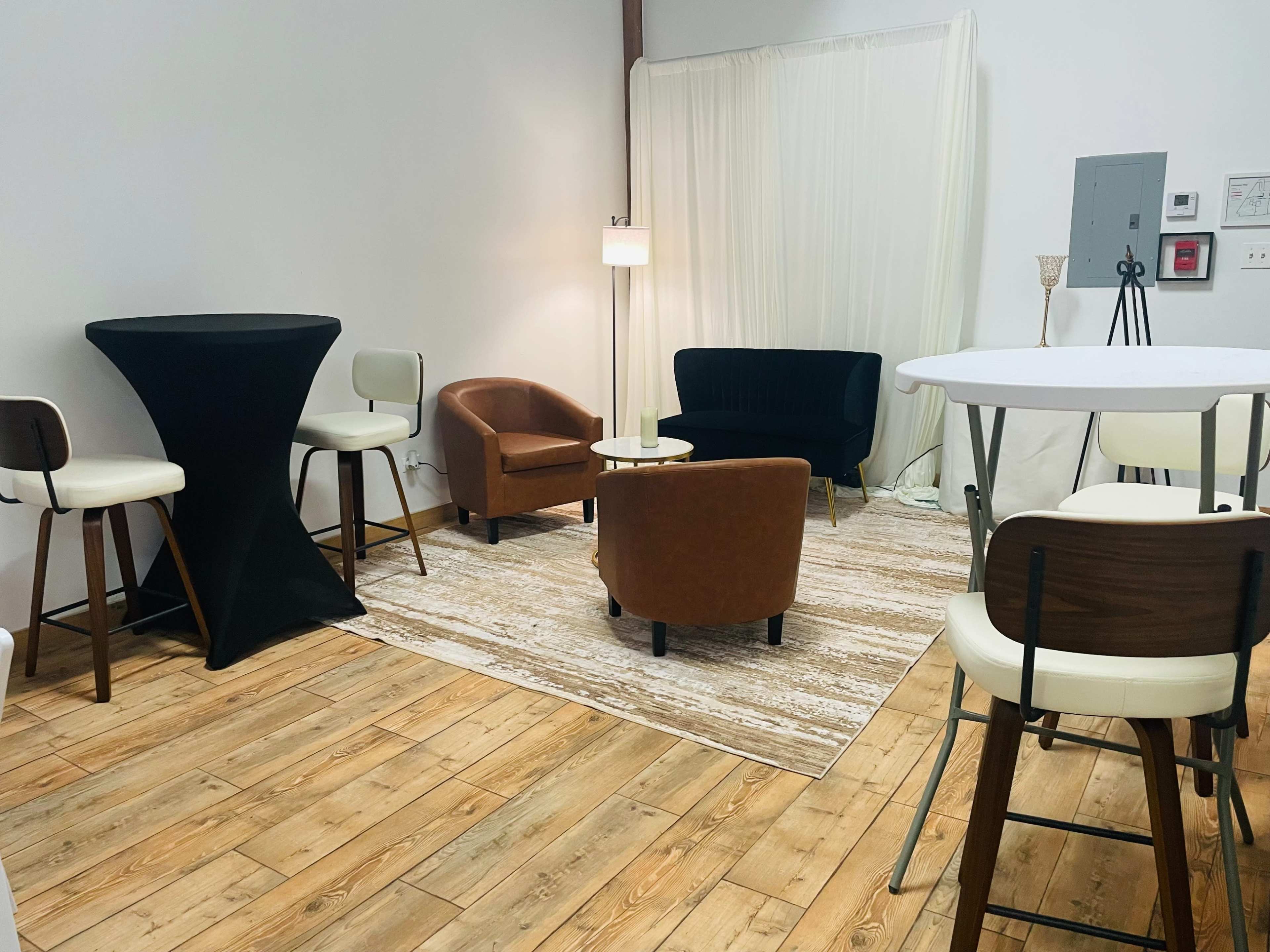 The image shows a small furnished room with various seating options, a large rug, and a light fixture.