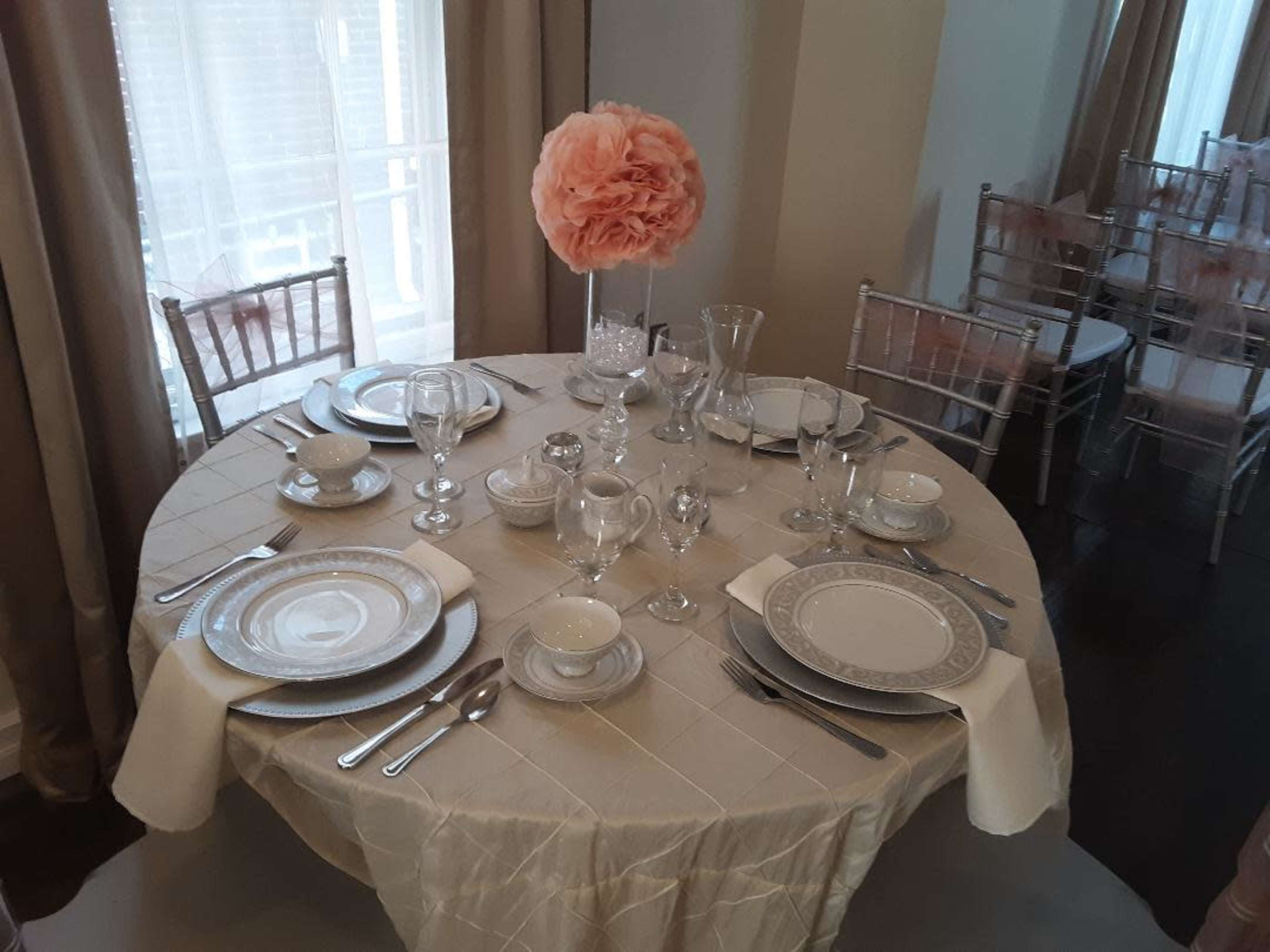 A round table is set with elegant dinnerware, glassware, and a large floral centerpiece.