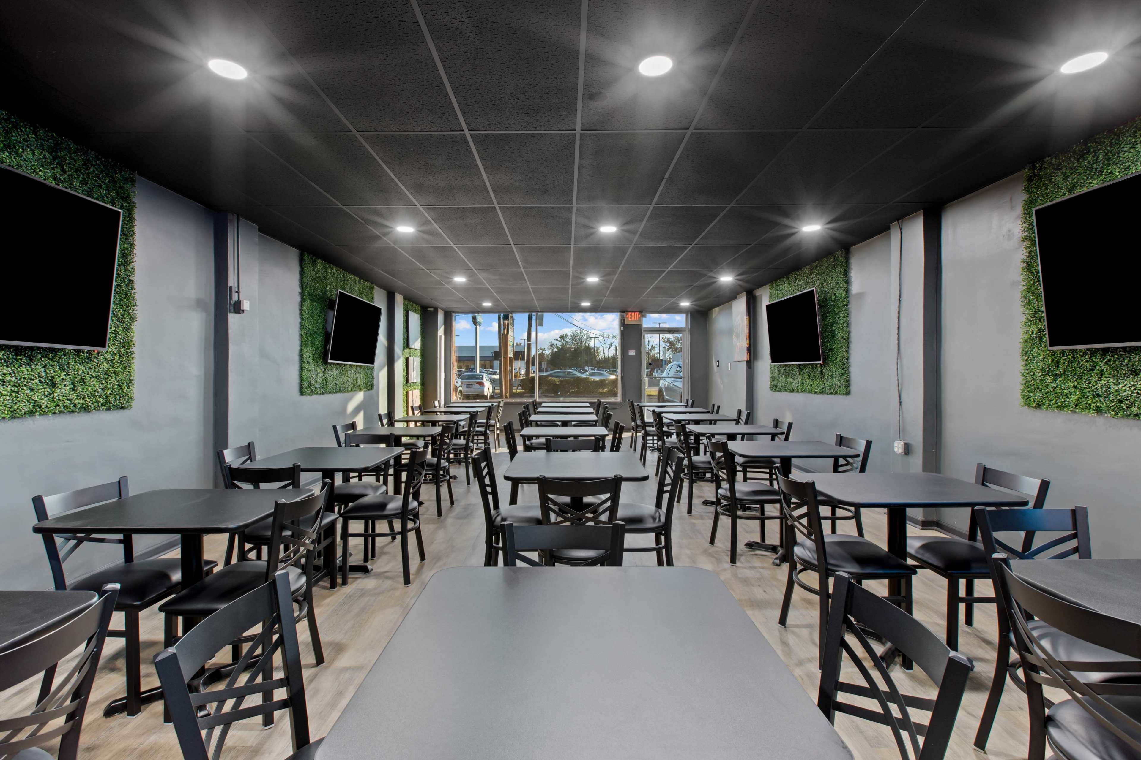 A spacious dining area with black tables and chairs, surrounded by green wall accents and large screens mounted on the walls.