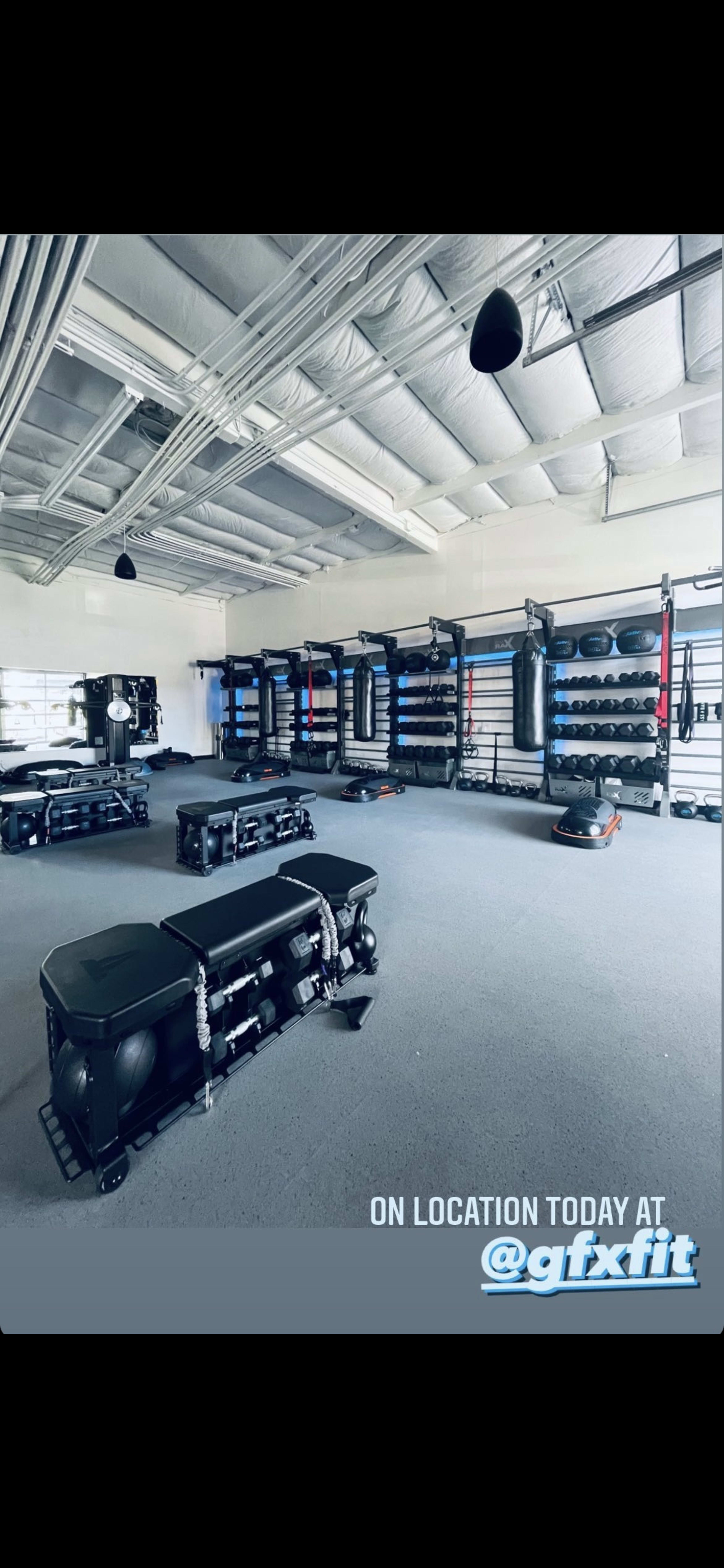A well-equipped fitness studio featuring various workout equipment, including benches, weights, and punching bags, arranged neatly against the walls.