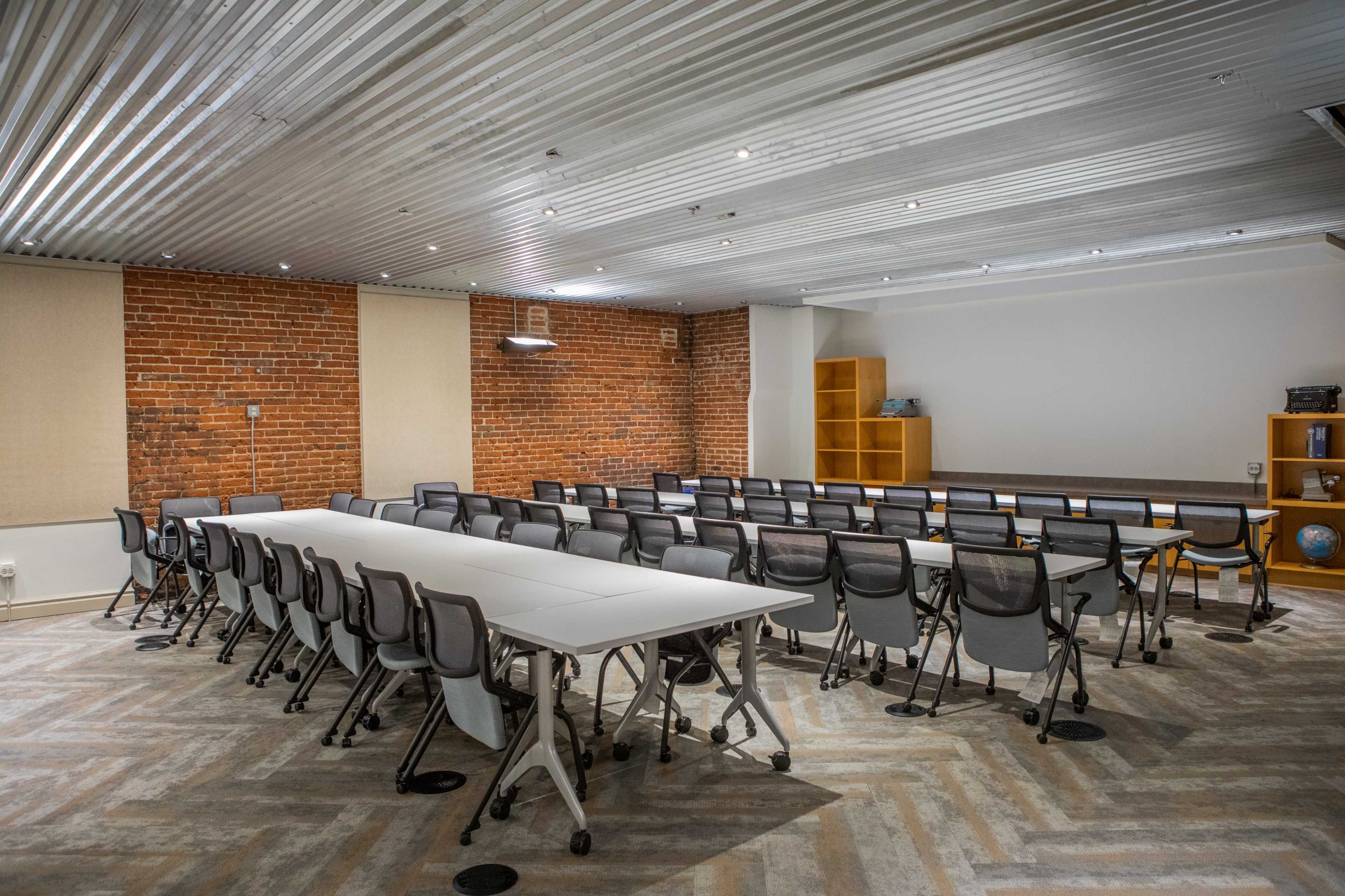 A modern conference room with a long table surrounded by black chairs, exposed brick walls, and a metal ceiling.