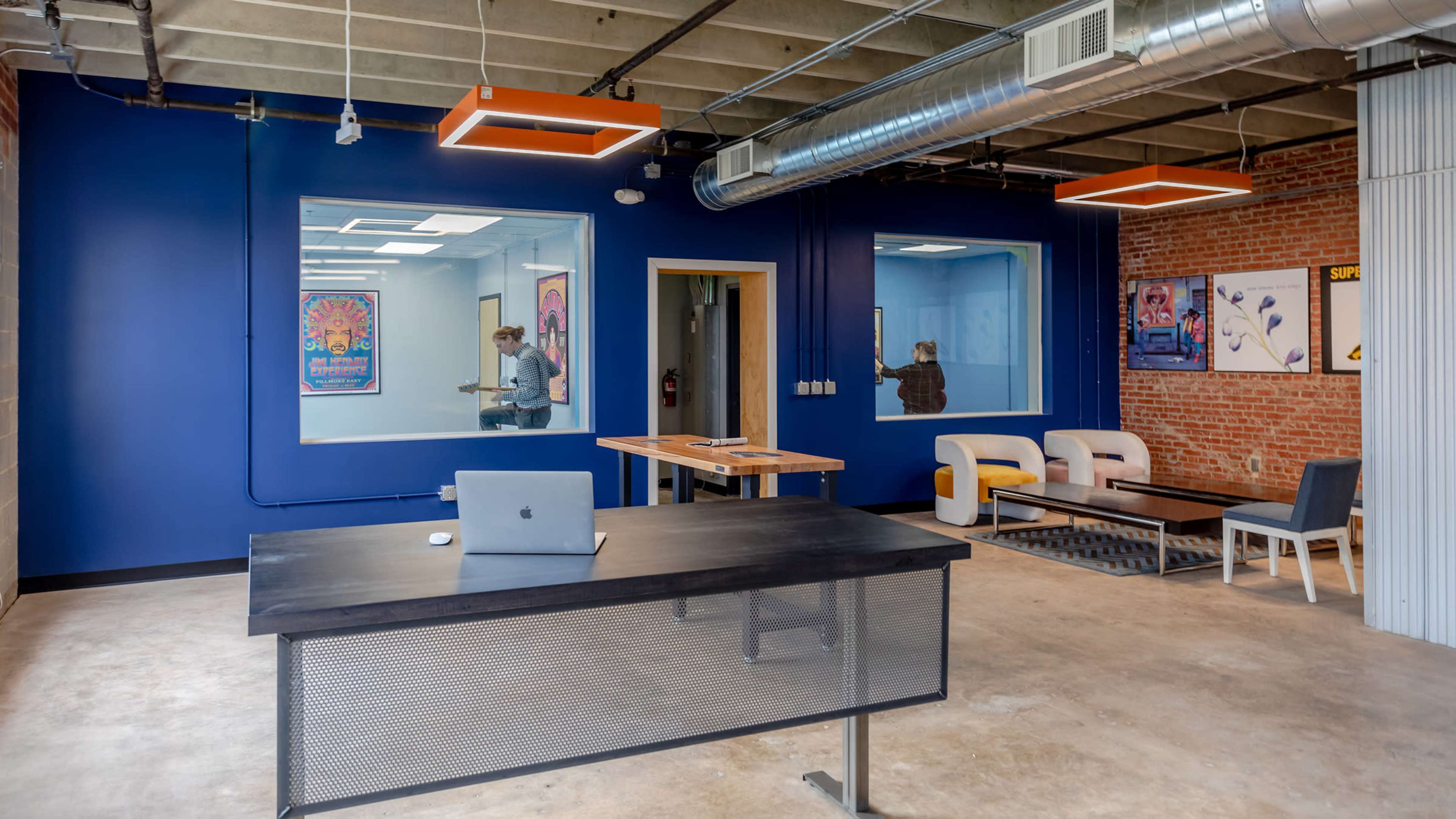 A modern office space with a black desk, several seating areas, and blue and brick walls.