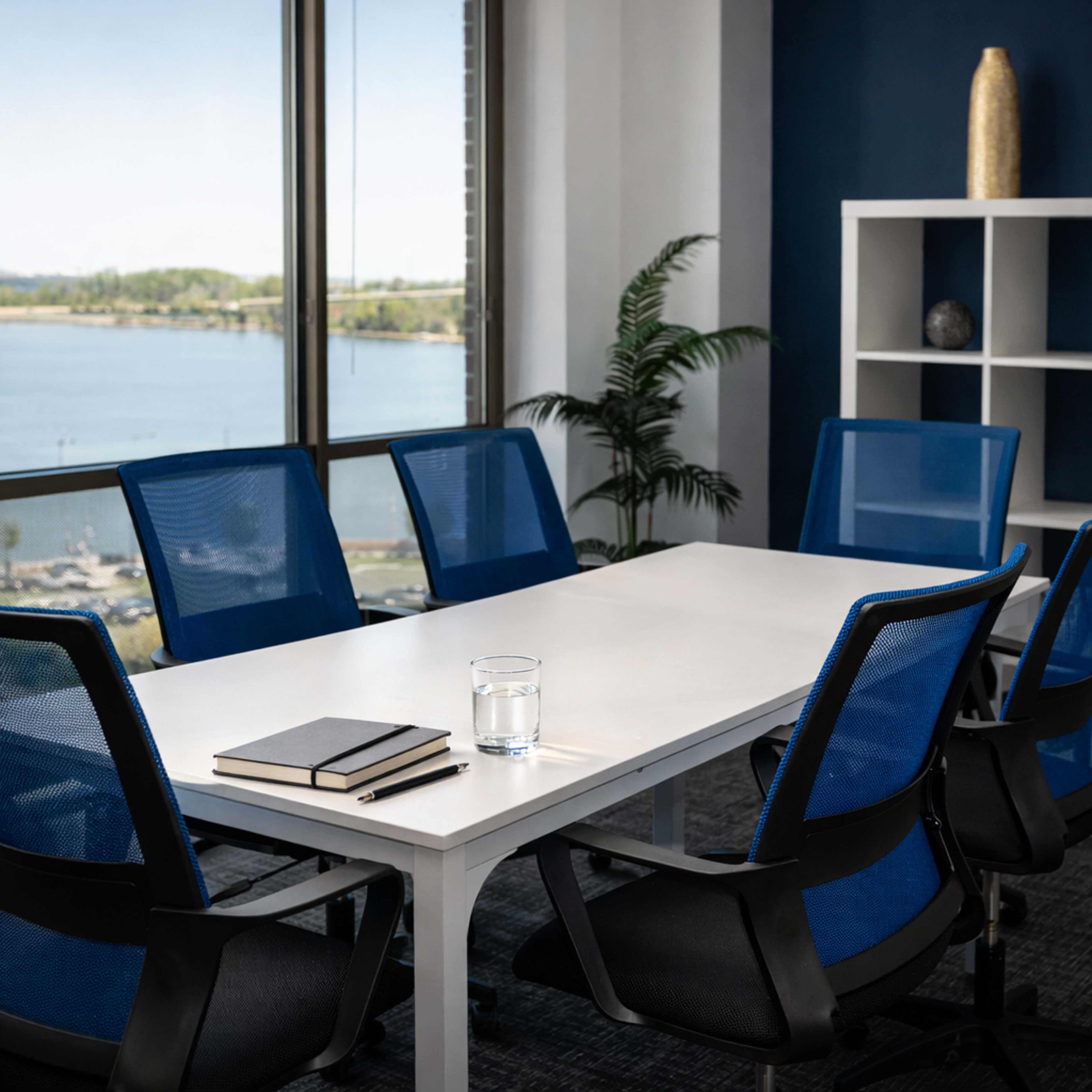 A modern conference room with a white table, blue chairs, and a view of a lake and greenery outside.