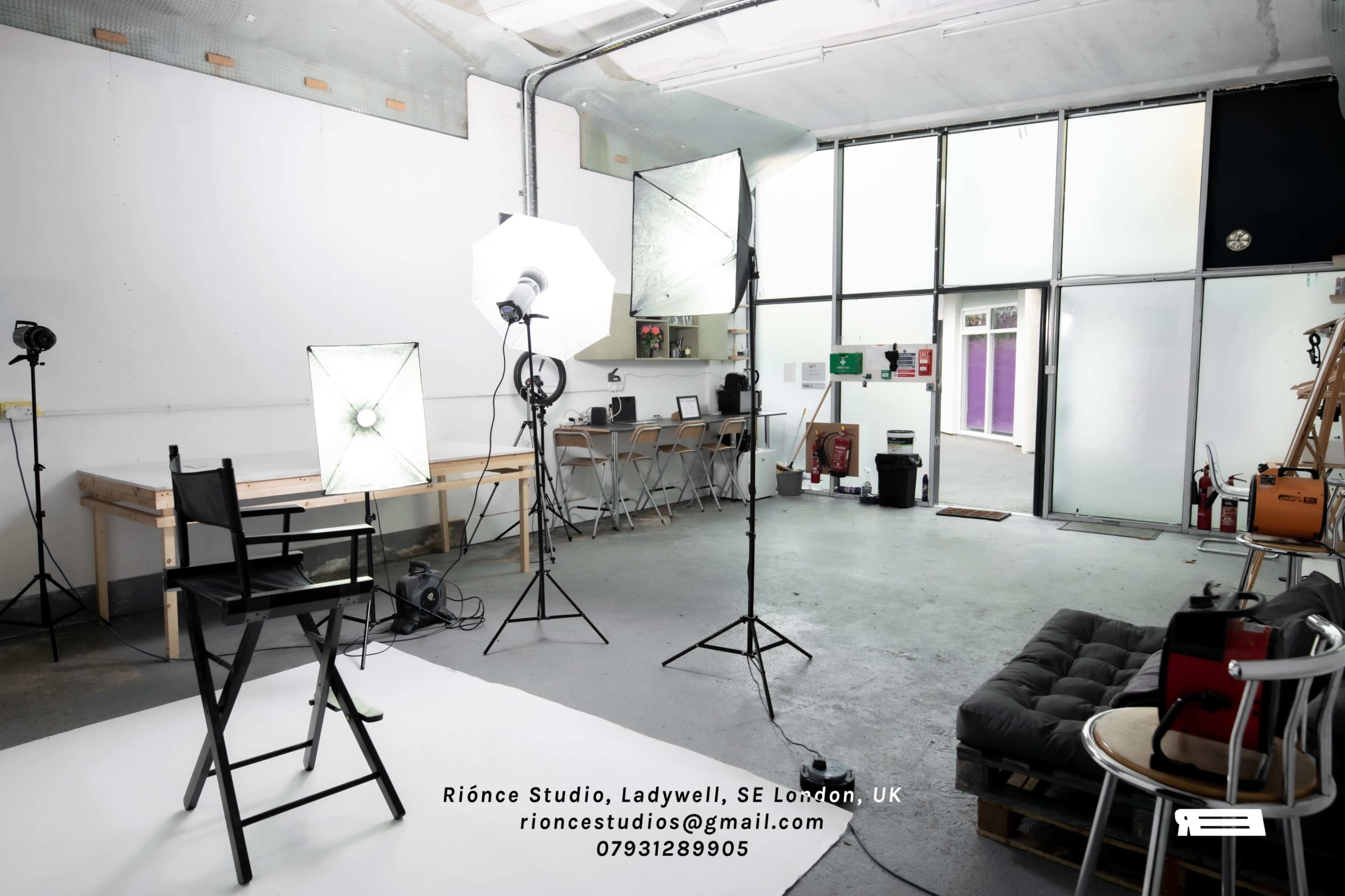 A photography studio with a backdrop, lighting equipment, a director's chair, and a sofa arranged in a spacious, well-lit environment.