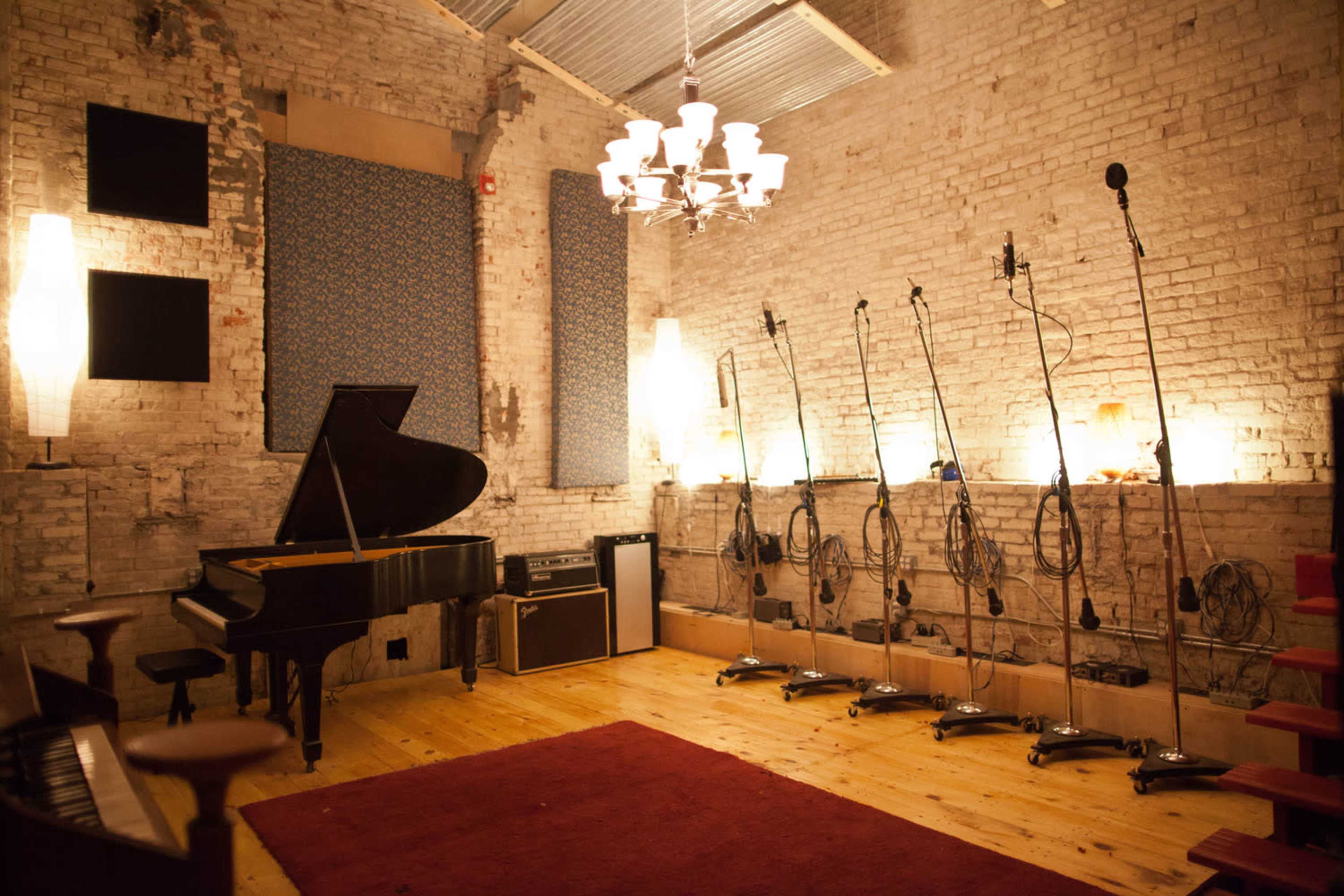 A music recording studio featuring a grand piano, several microphone stands, and a well-lit brick wall.