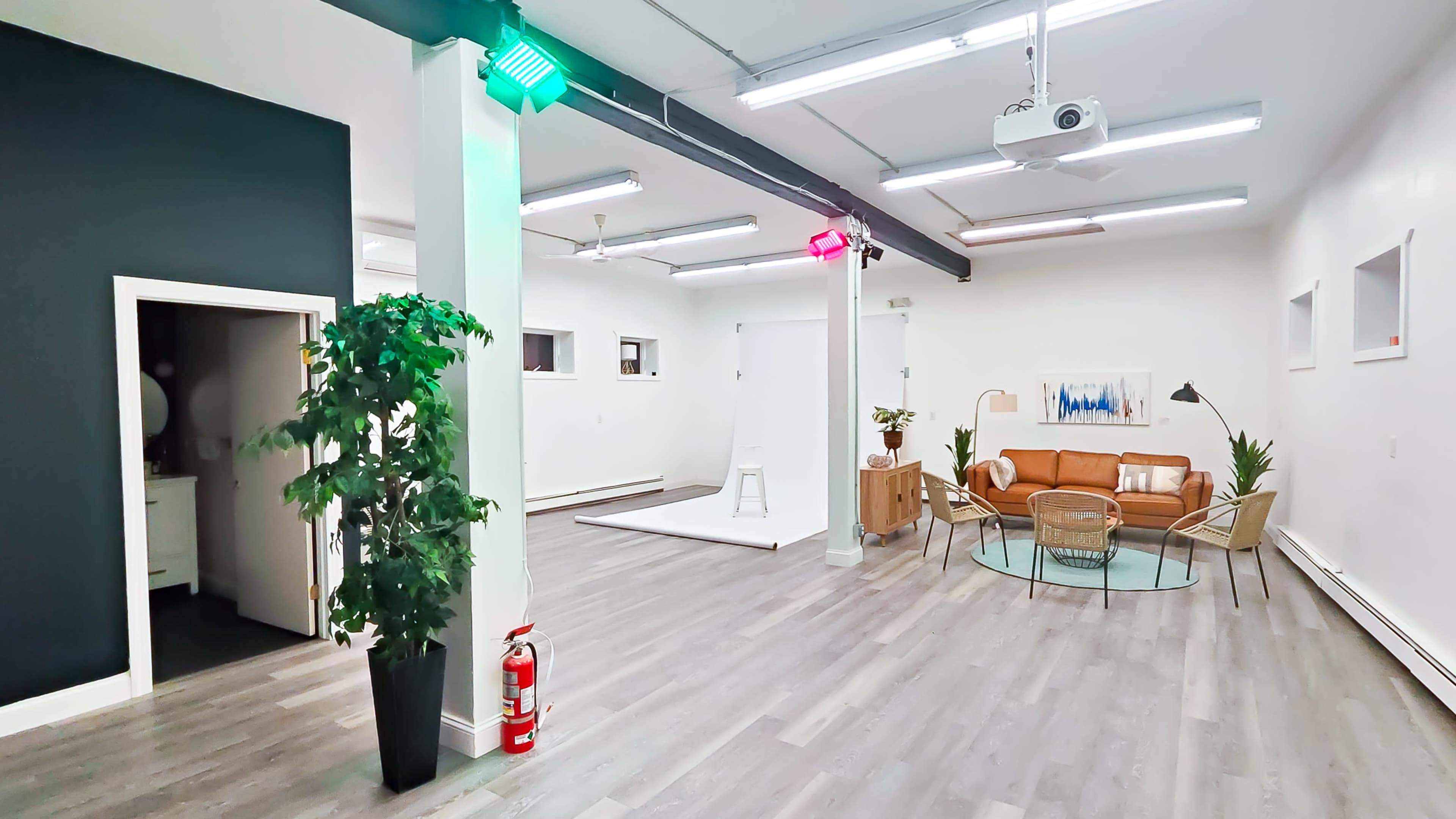 A modern interior space featuring a seating area with a brown couch, a coffee table, a small stage, and green and red lights illuminating the room.